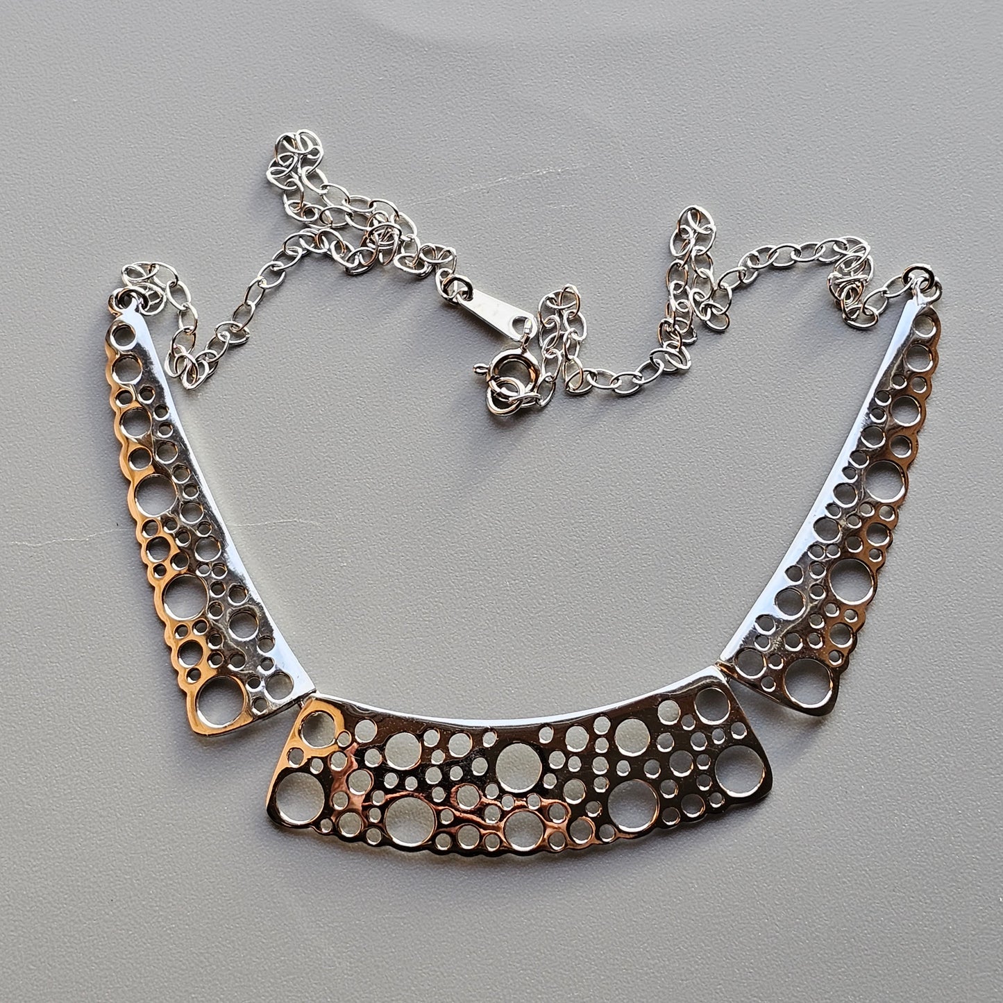 Silver necklace with a curved pendant featuring circular cutout patterns.