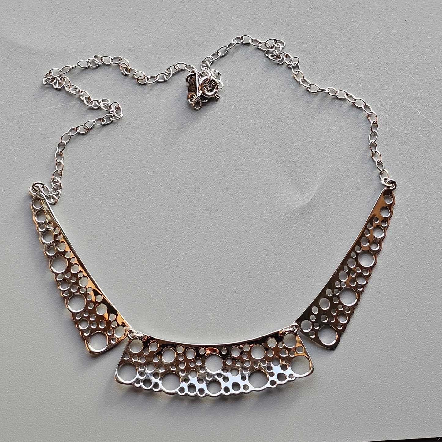 Silver necklace with a curved pendant featuring circular cutout patterns.