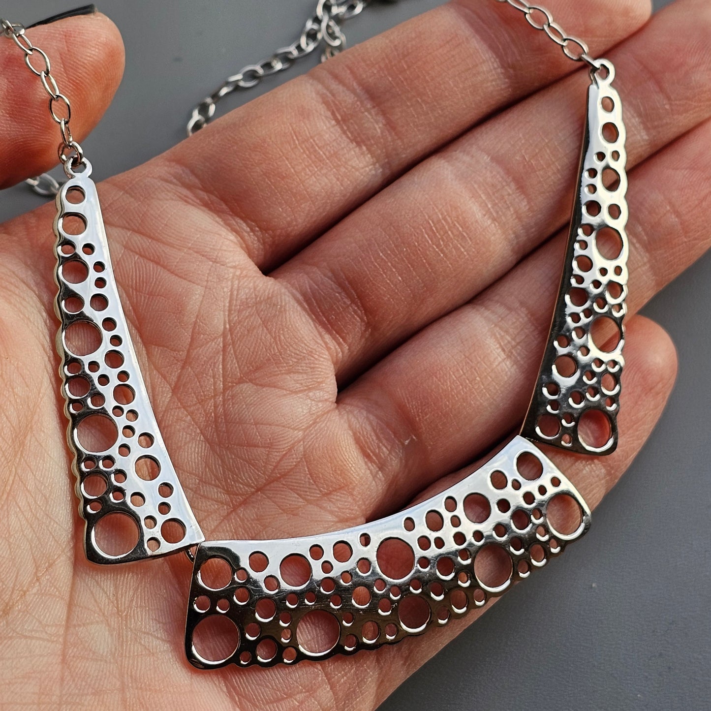 Silver necklace with a perforated crescent-shaped pendant featuring circular cutouts of varying sizes.