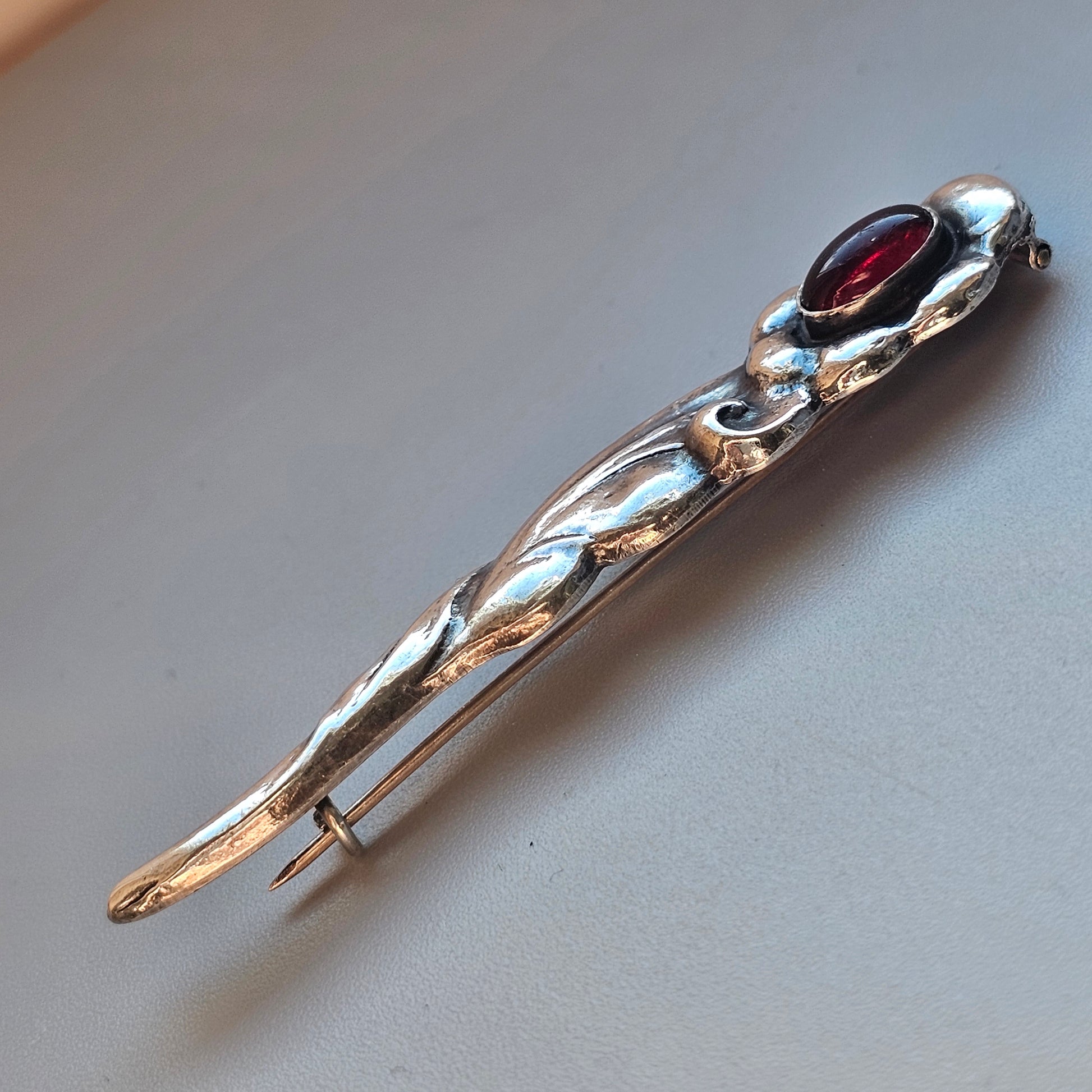 Silver brooch or pin with a red gemstone at one end and an elongated, twisted design.