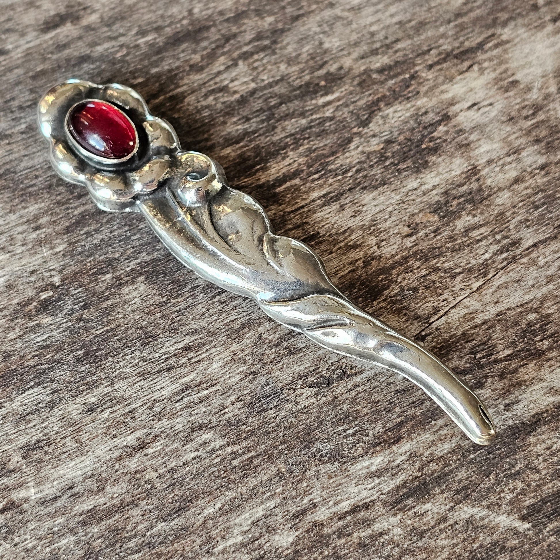 Silver flower-shaped brooch with a red gemstone center.