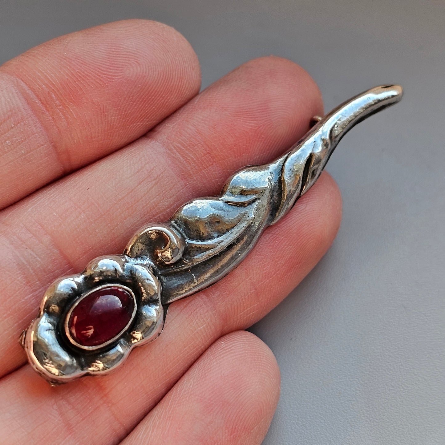 Silver pendant with a curved leaf-like design featuring a red gemstone.