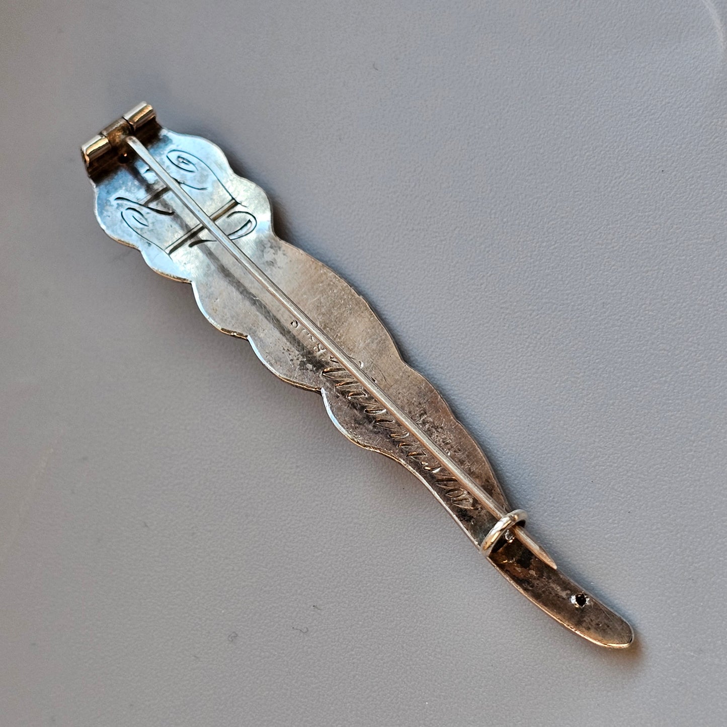 Decorative metal feather-shaped bookmark or page marker with a blue enamel accent.