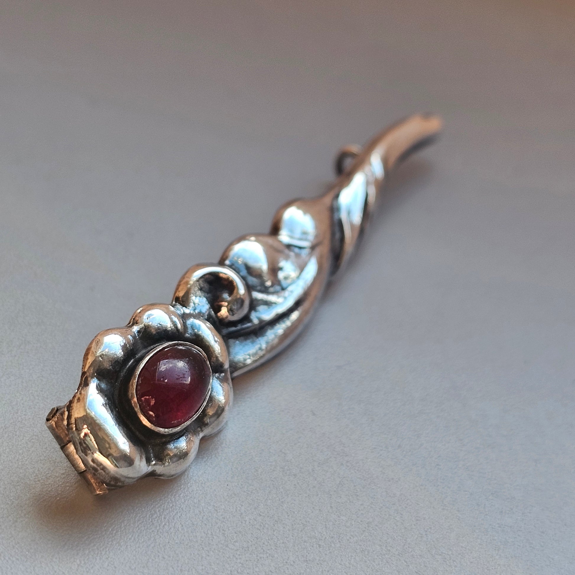 Ornate silver brooch or pin with a red gemstone centerpiece.