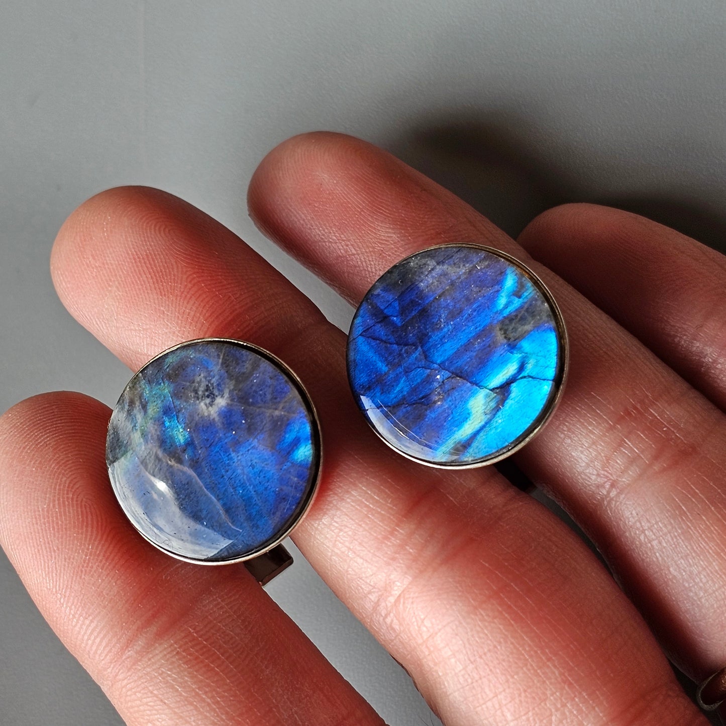 Two circular gemstones or cabochons with vibrant blue and iridescent coloring held between fingers.