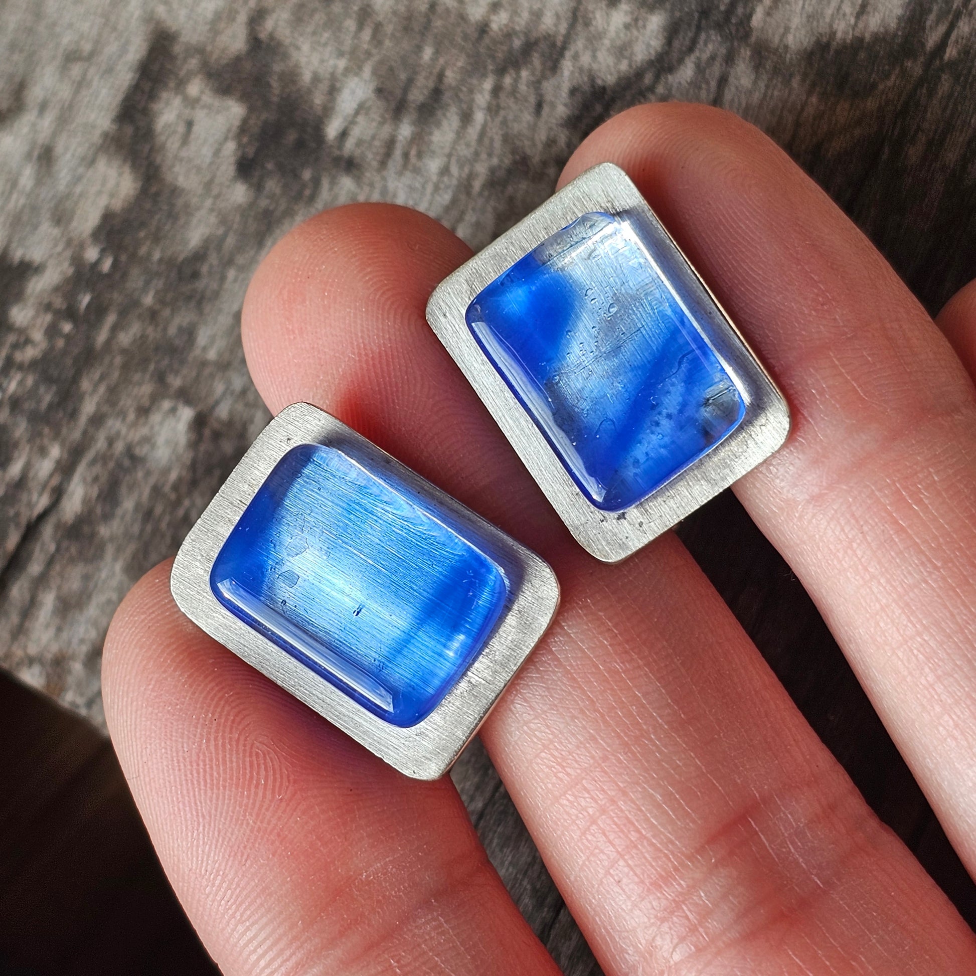 Two rectangular blue gemstones or glass pieces set in silver-colored metal frames.