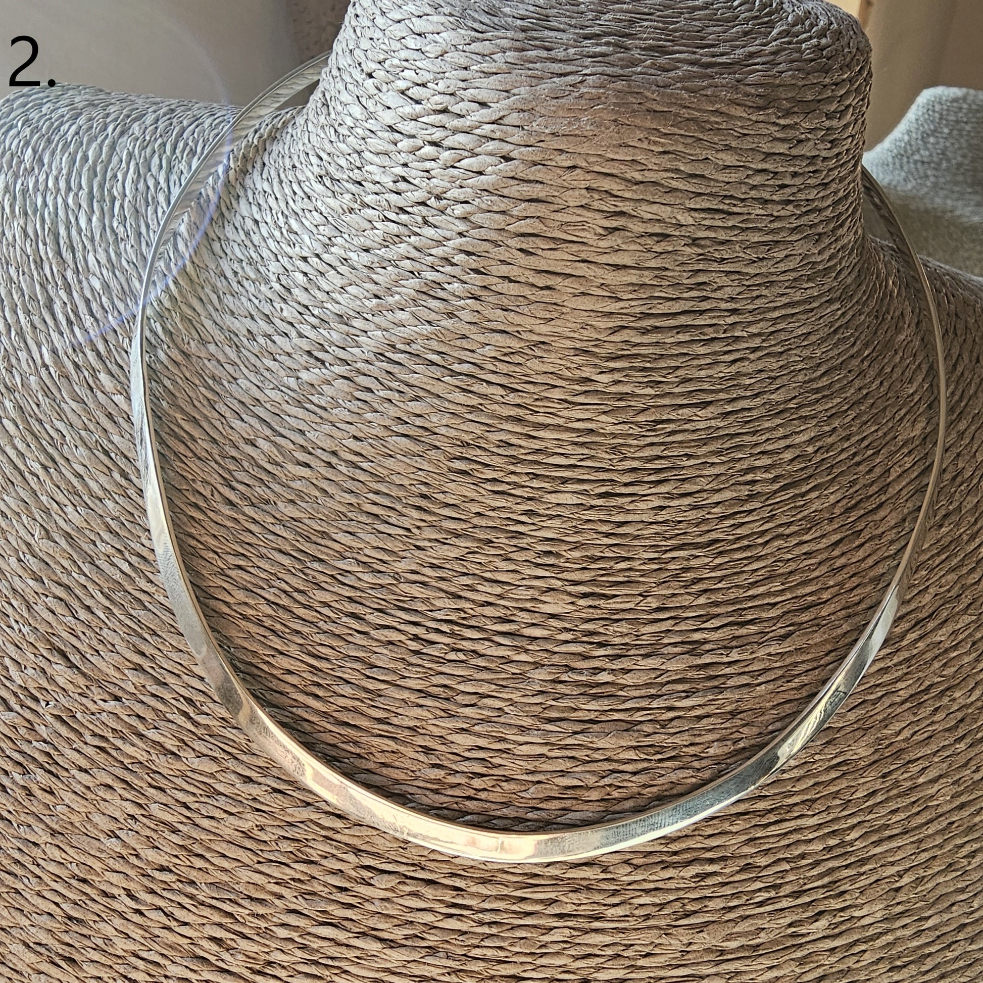 Woven straw sun hat with a silver necklace draped around it.