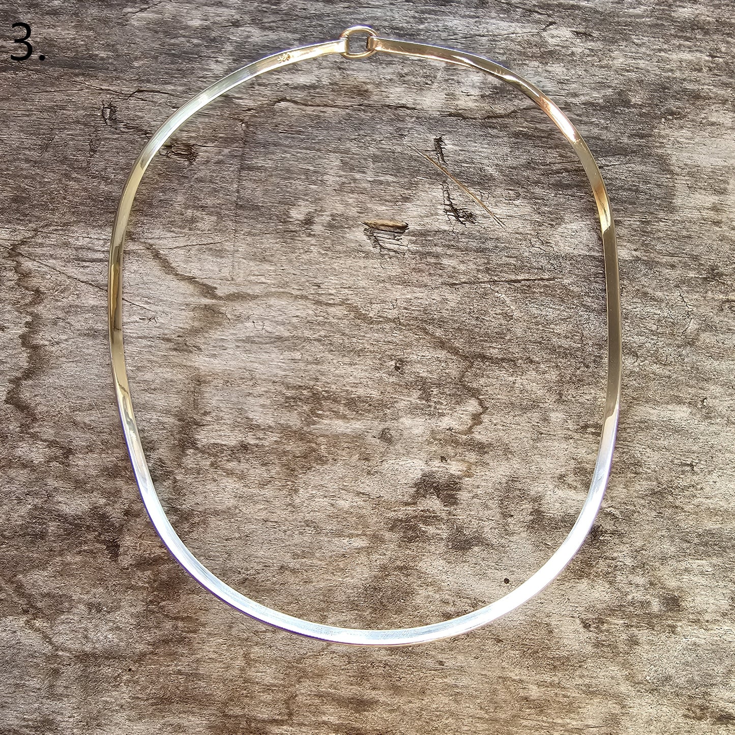 Thin, circular metal necklace or collar with a partial gold-colored section.