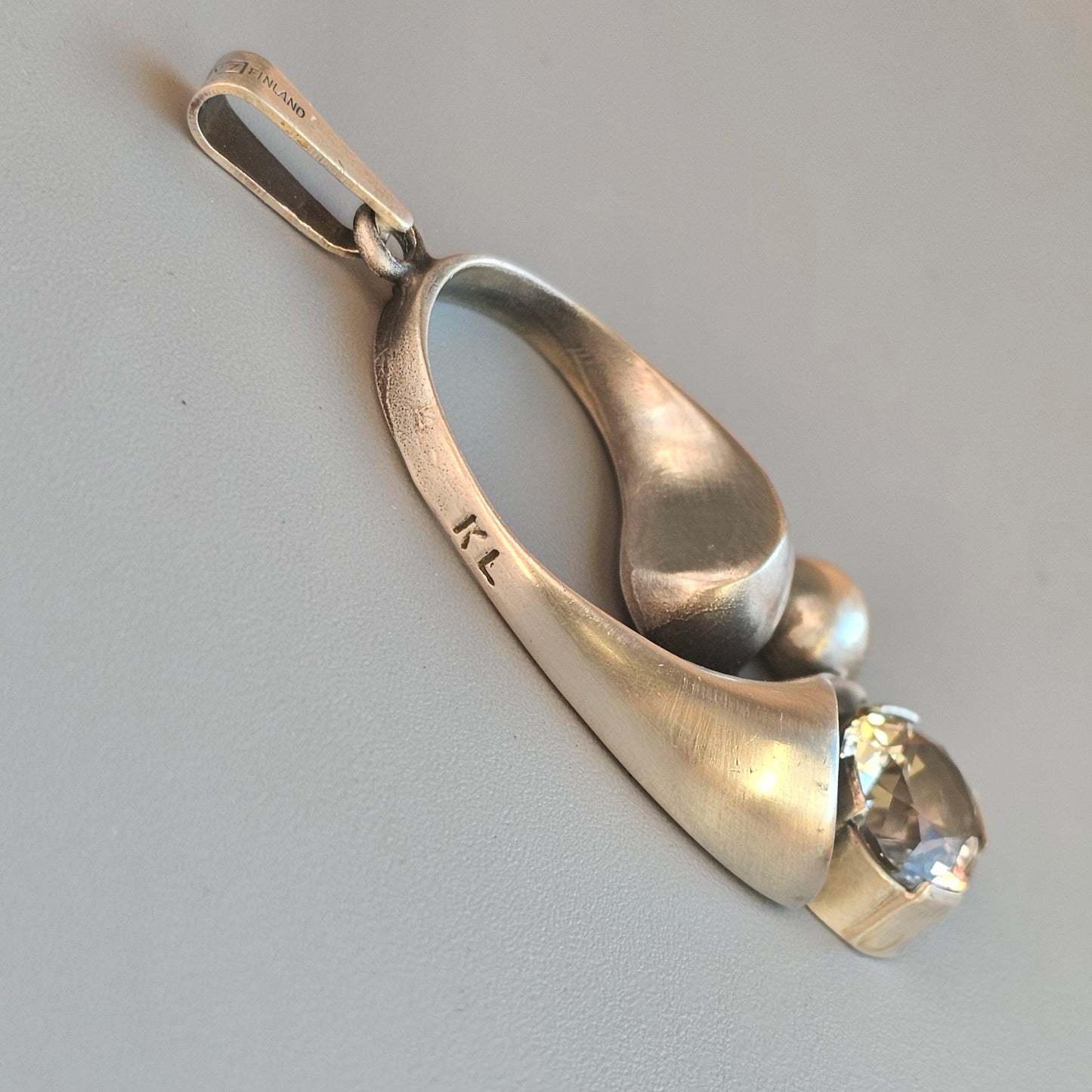 Silver pendant shaped like a stylized ballet shoe with a gemstone at the toe.