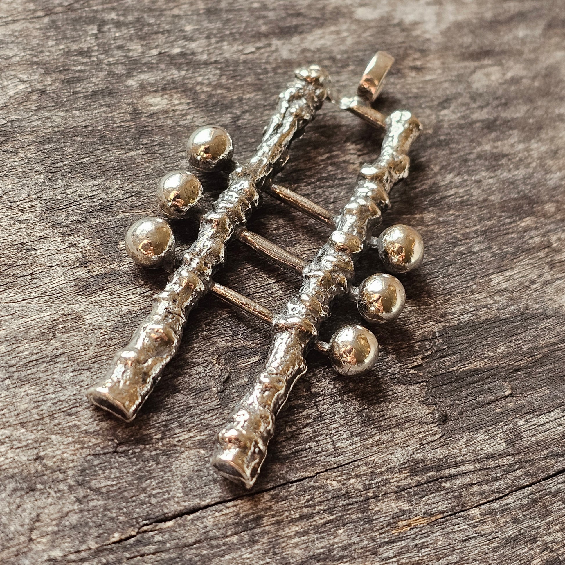 Silver pendant or charm shaped like a stylized human figure with spherical joints.