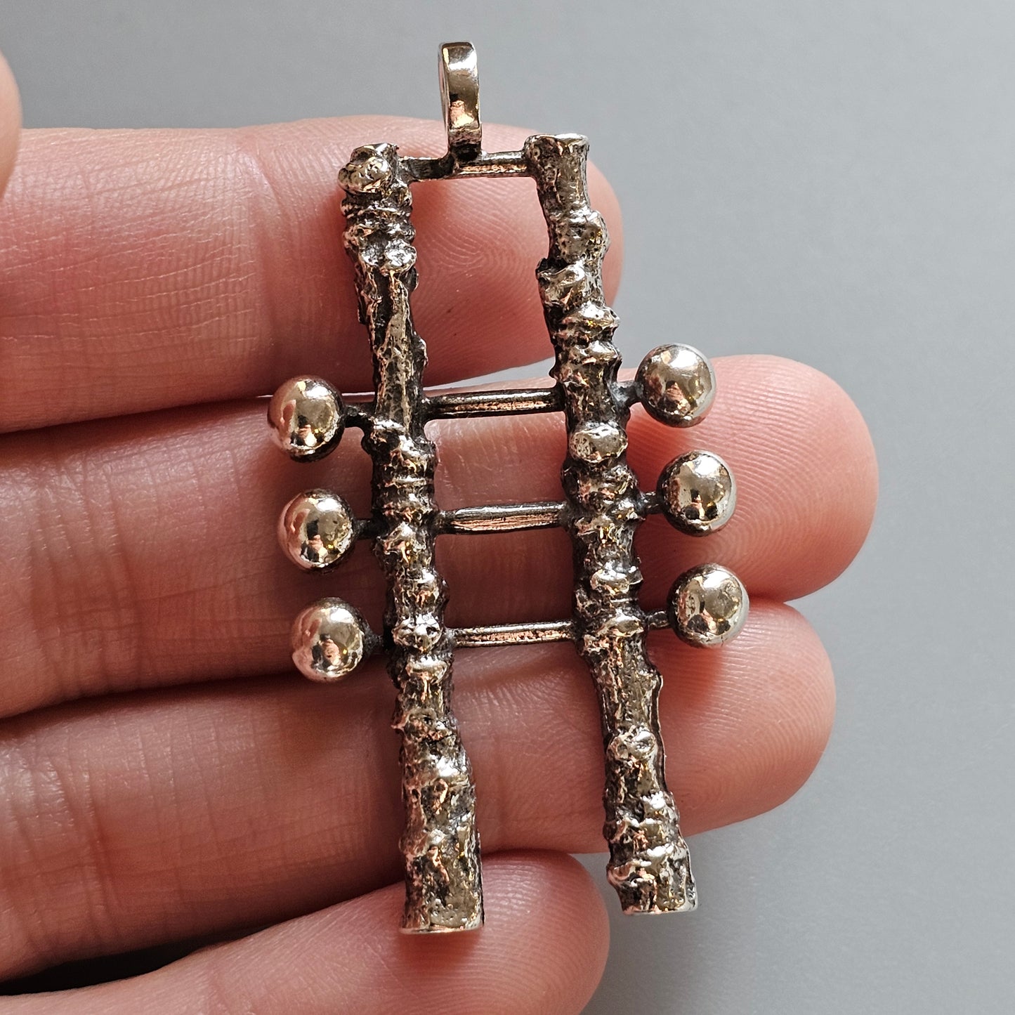 Silver pendant shaped like a ladder with spherical ornaments on one side.