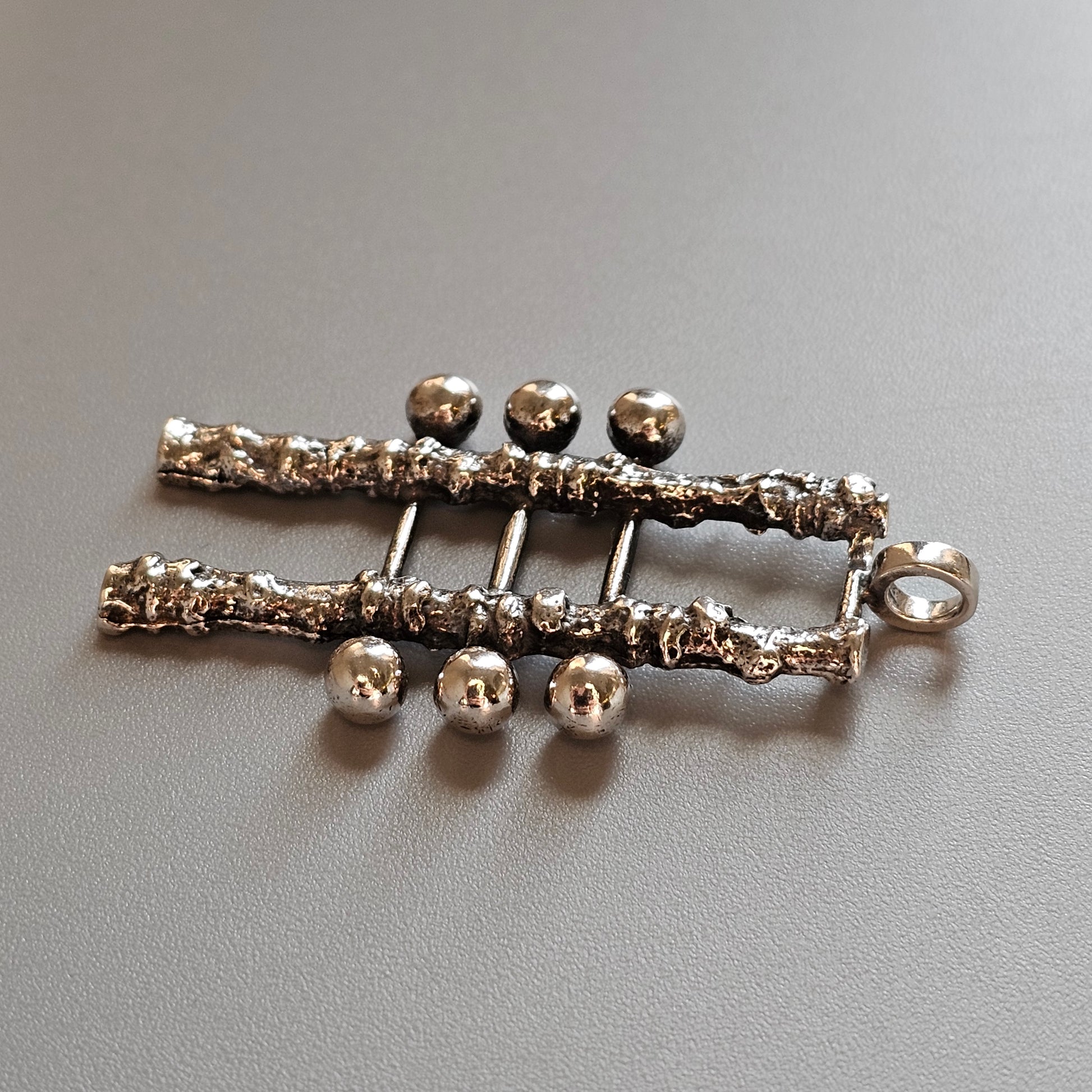 Silver-toned brooch or pin shaped like a skeletal hand with six spherical fingertips.