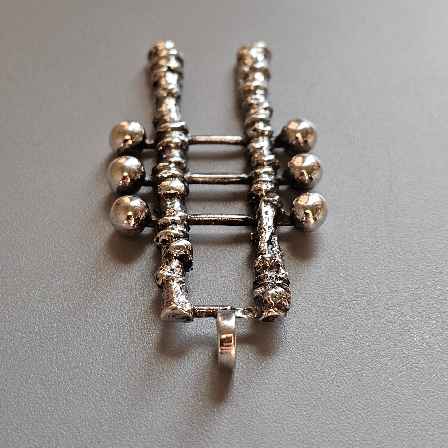 Silver-toned metal brooch or pin shaped like a ladder with decorative spheres.