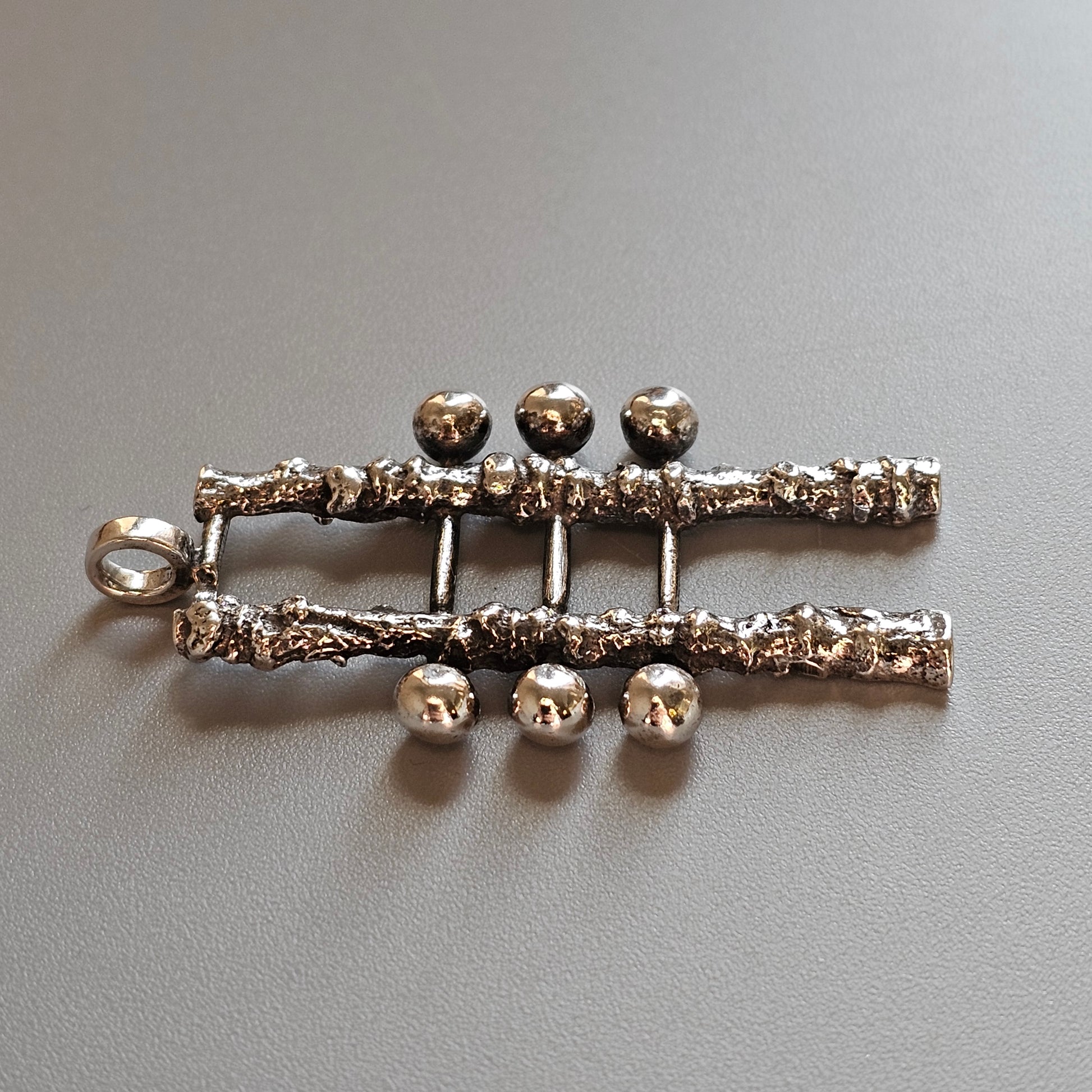 Silver-toned metal brooch or pin with a skeletal spine design and decorative spheres.