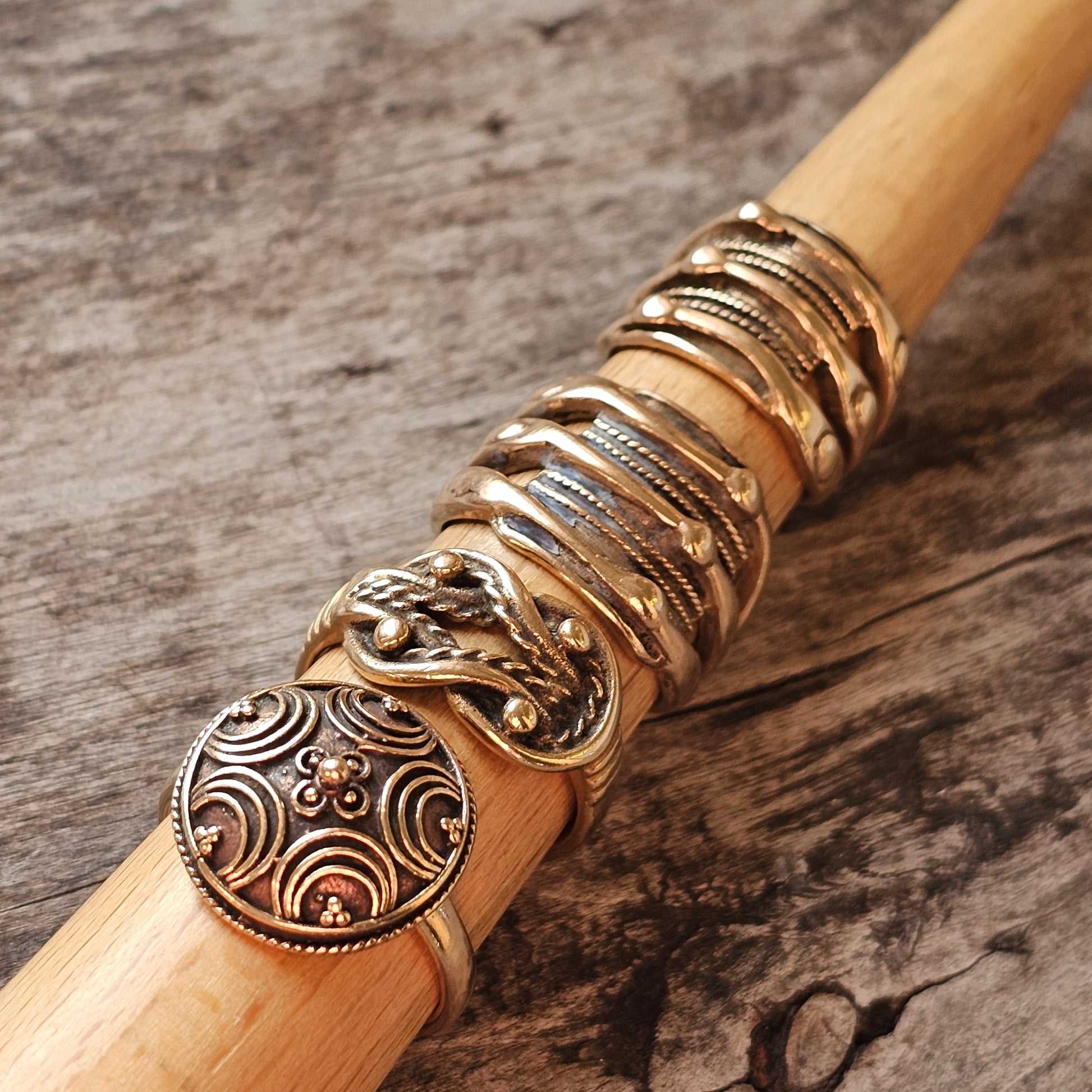 Wooden walking stick adorned with ornate metal rings and a decorative circular pendant.