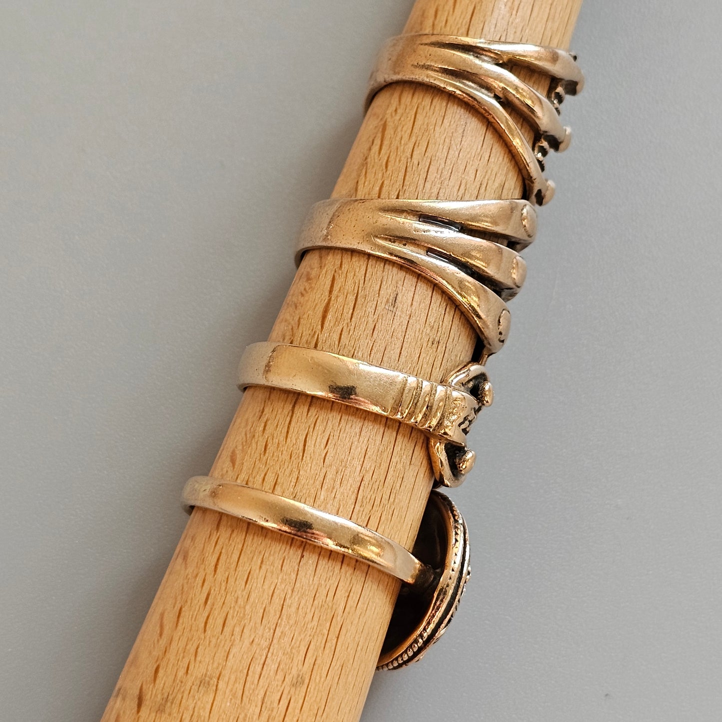 Wooden dowel or rod with several gold rings wrapped around it.