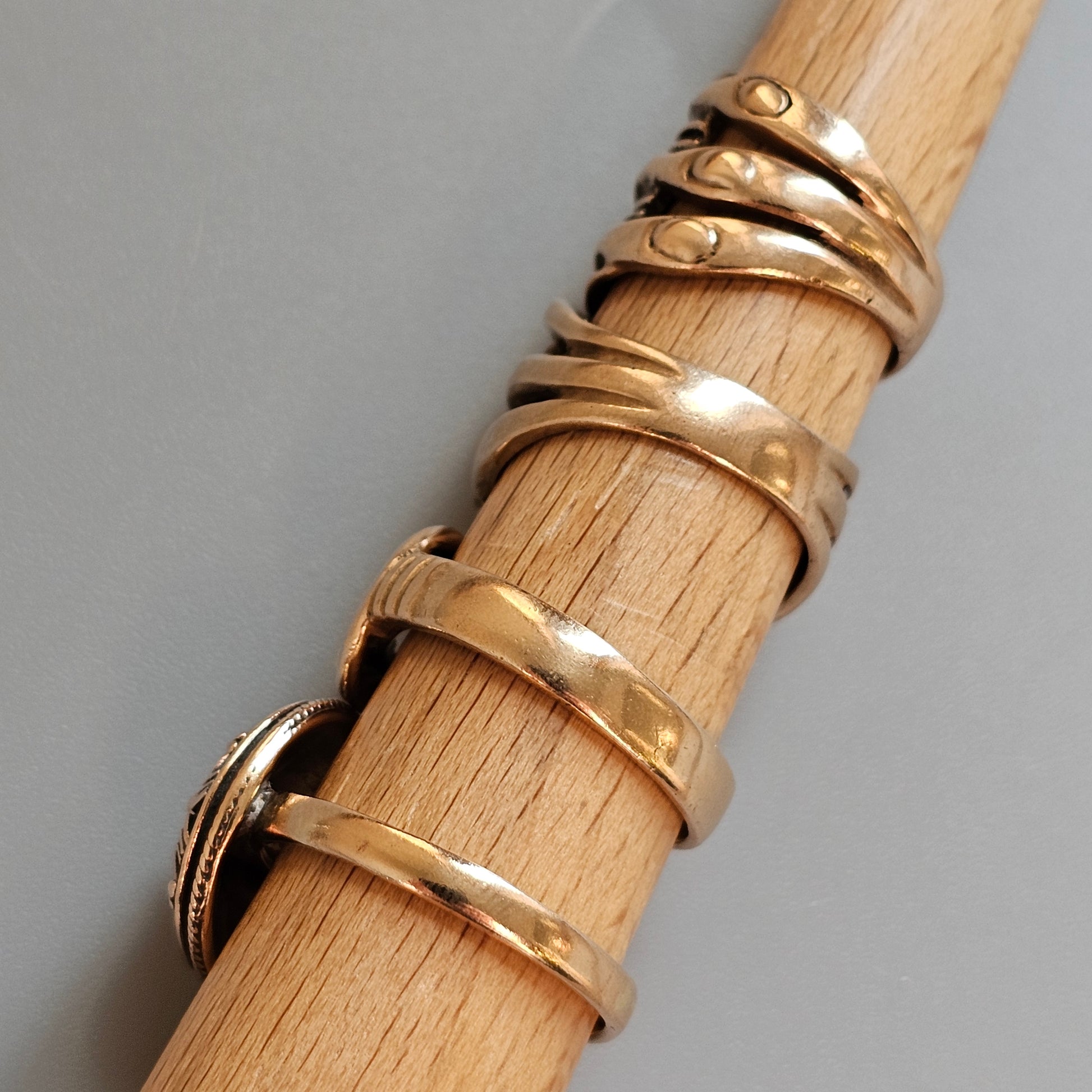 Wooden dowel or rod with multiple gold rings wrapped around it.