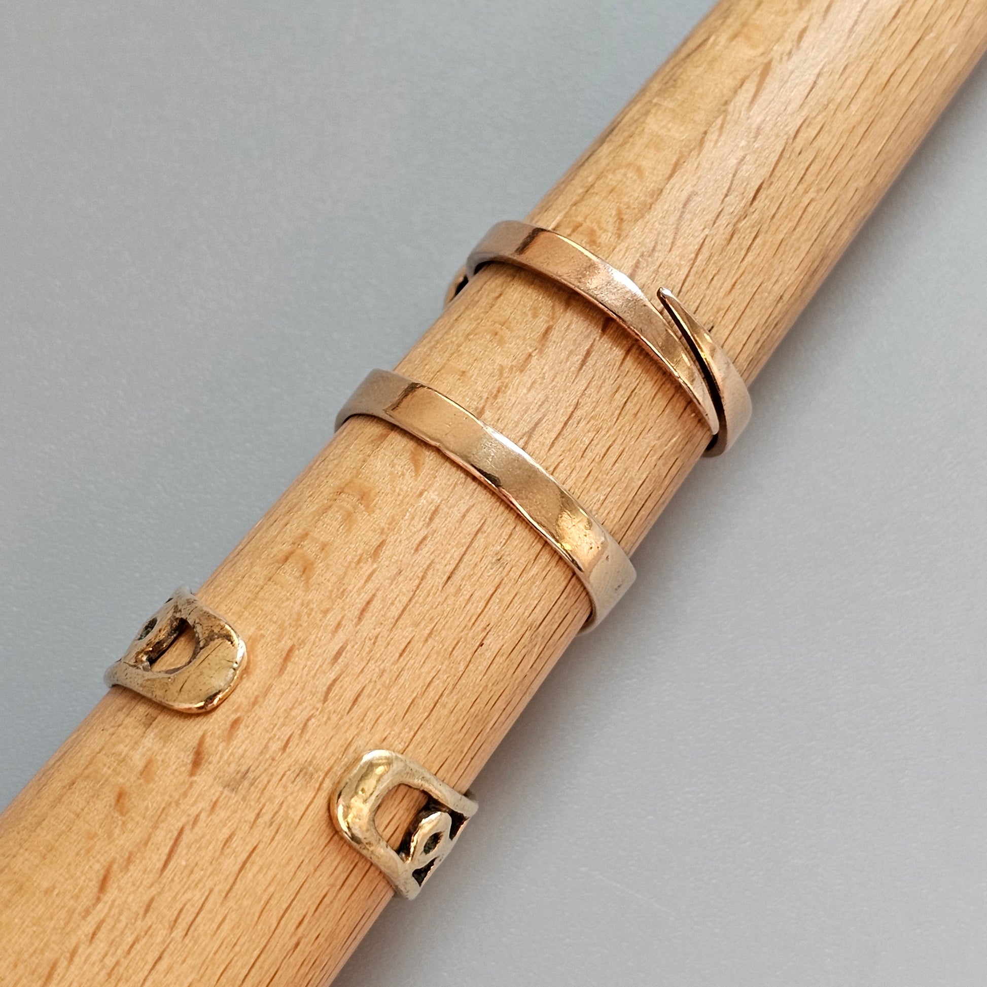 Wooden dowel or rod with several gold-colored rings wrapped around it.