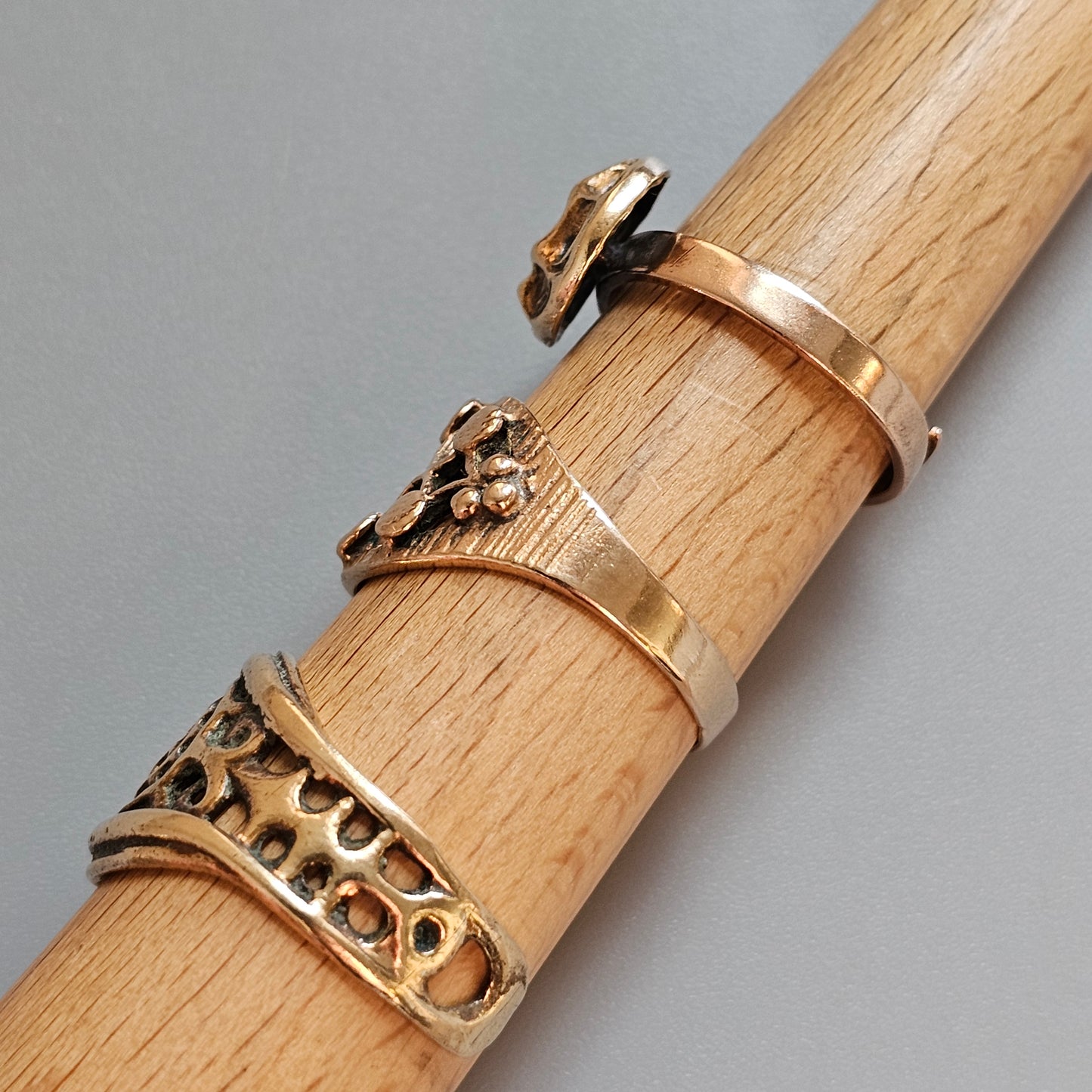 Wooden dowel or rod with three gold rings of different designs wrapped around it.