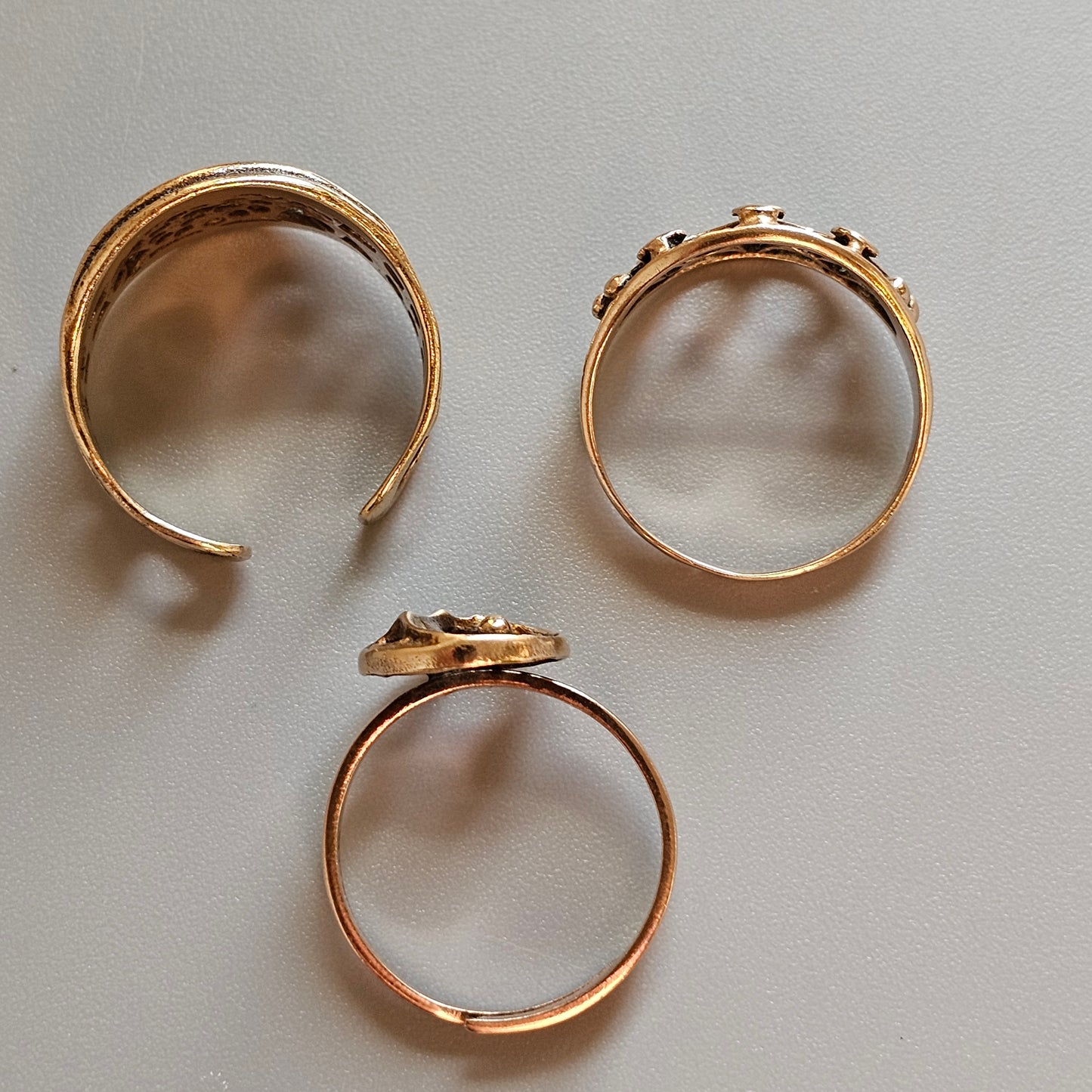 Three gold-colored rings, two open and one closed, arranged on a surface.