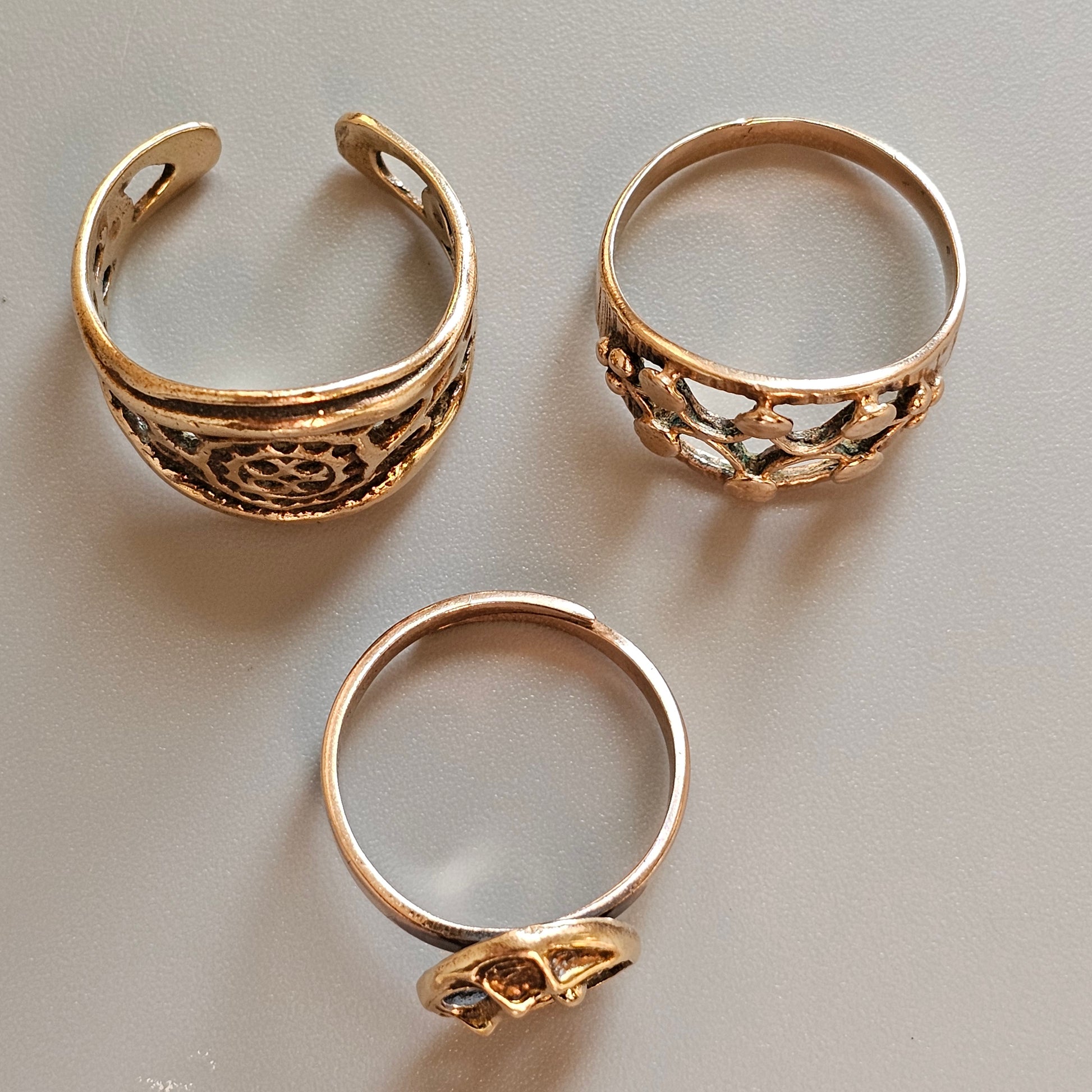 Three gold-toned rings with decorative patterns and designs.