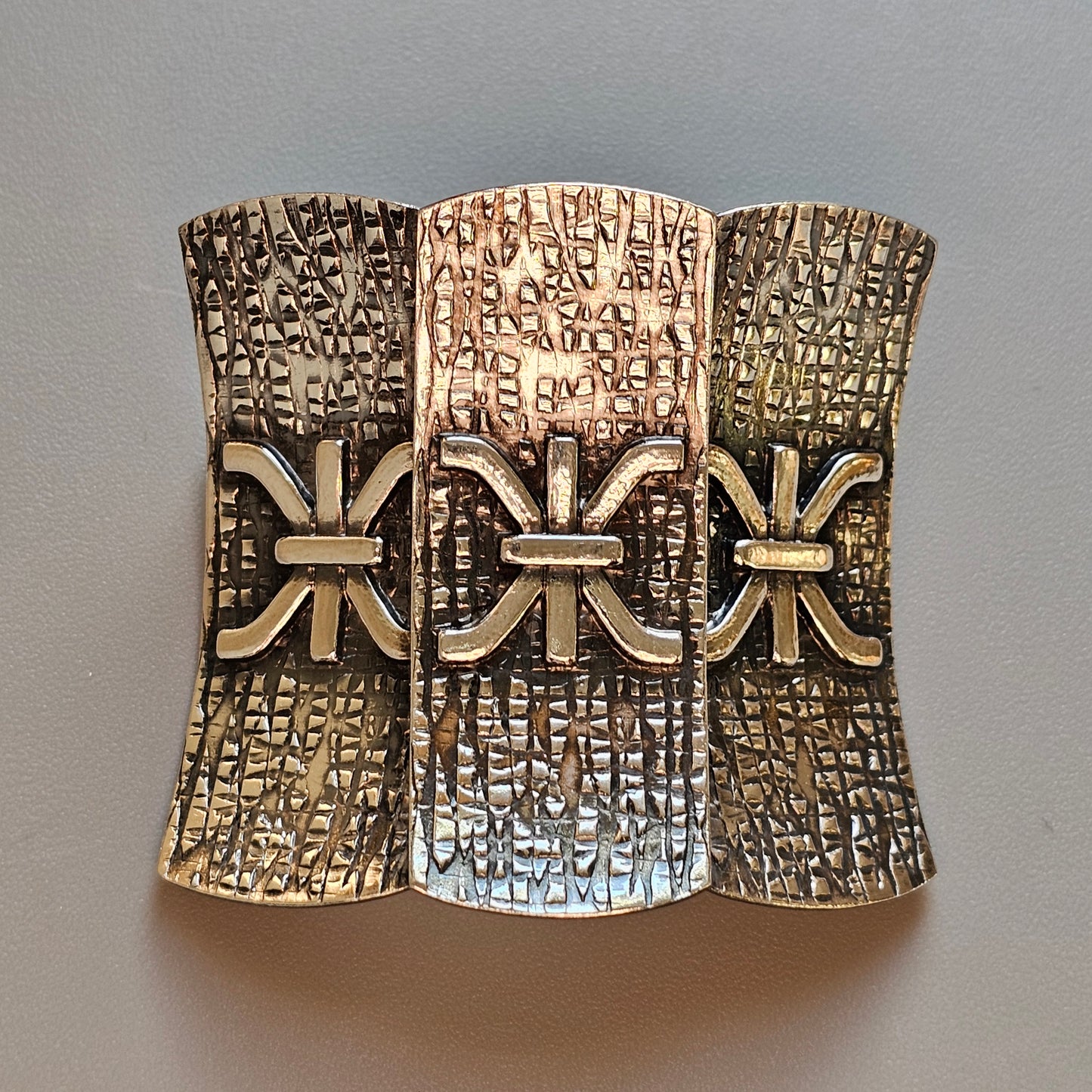 Ornate metal cuff bracelet with three sections featuring intricate engraved patterns and decorative bow-like elements.