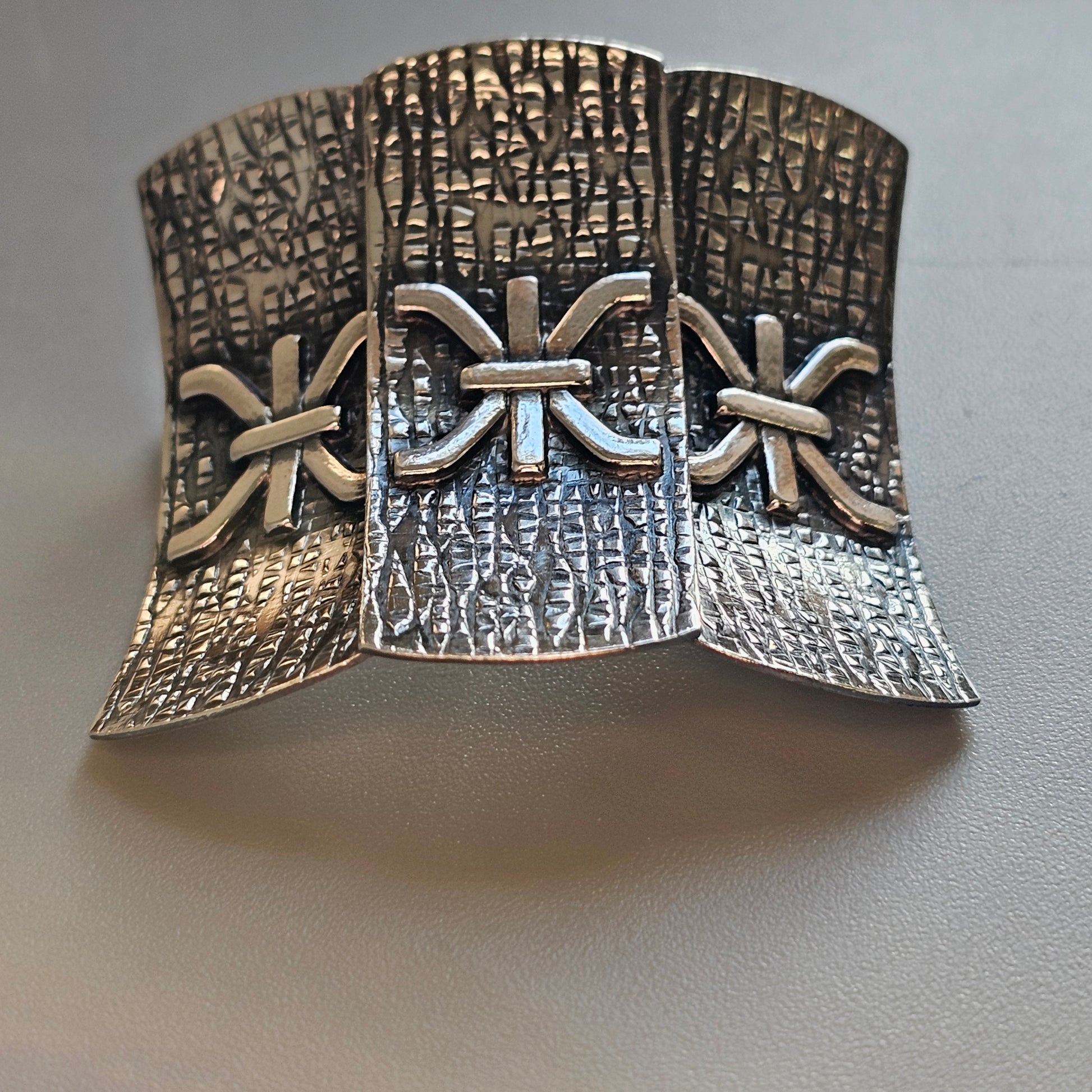 Ornate silver cuff bracelet with textured patterns and decorative cross-like designs.