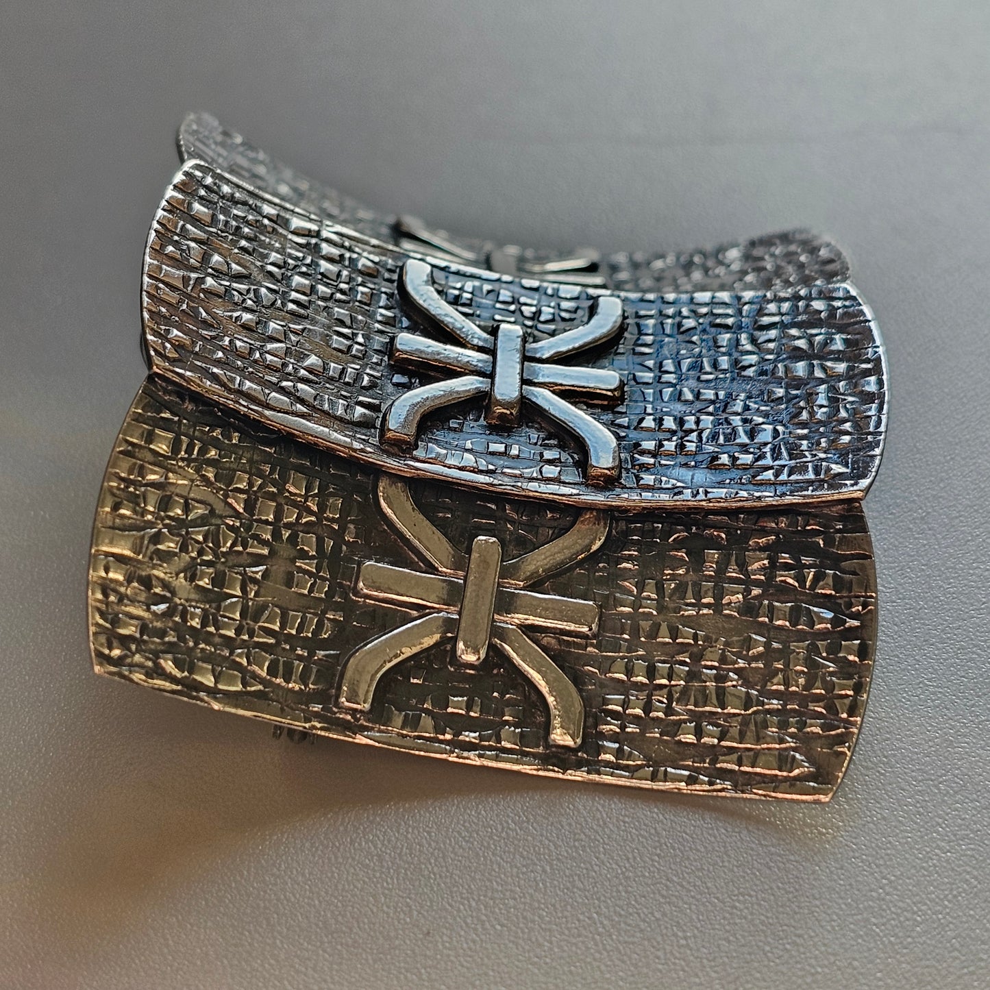 Ancient-looking metal artifact with inscribed symbols and decorative bow-like shapes.