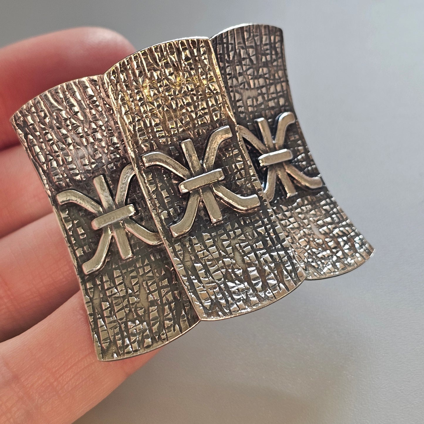 Ornate metal brooch or pin with three textured panels and decorative fleur-de-lis designs.