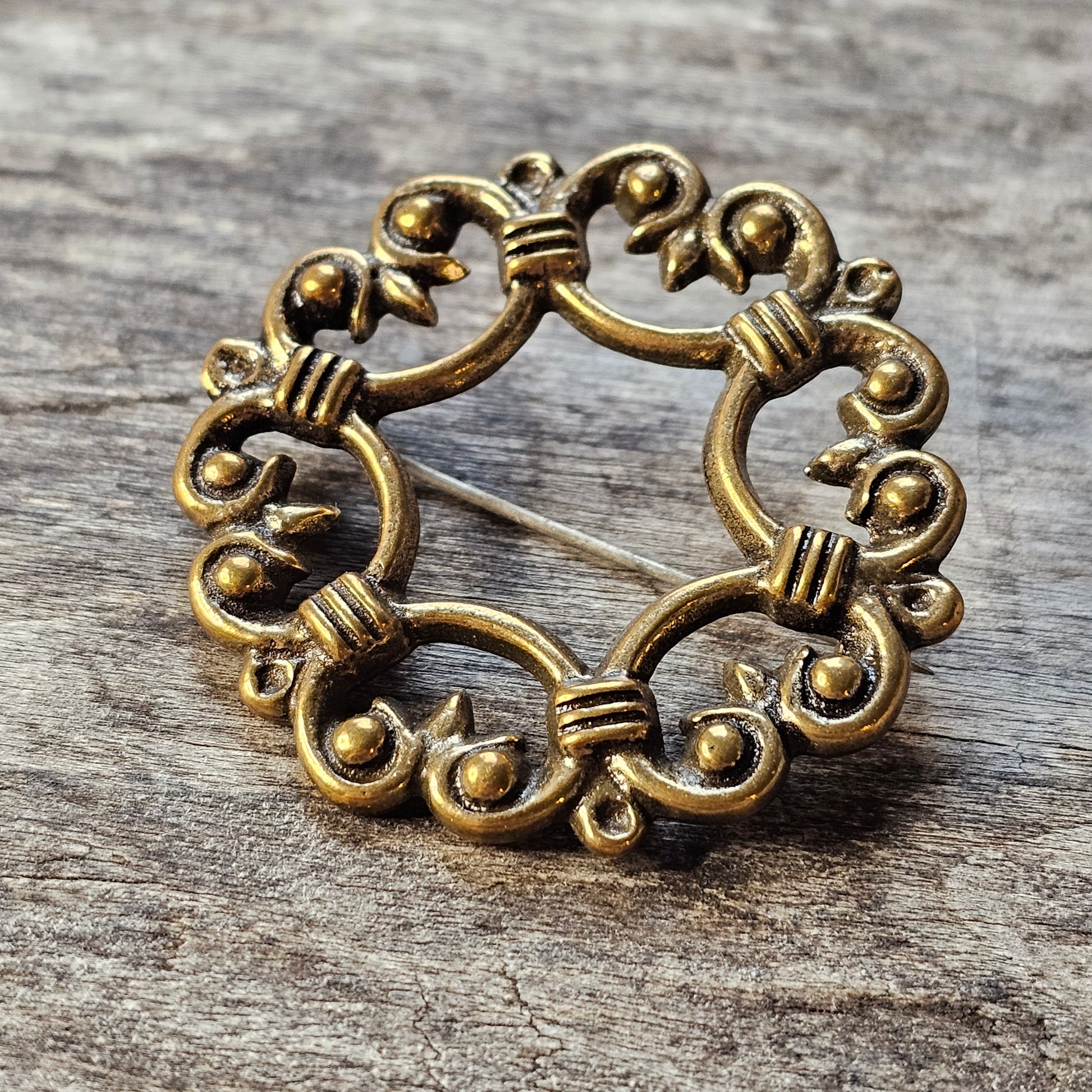 Ornate circular gold-toned metal brooch with intricate scrollwork and bead details.