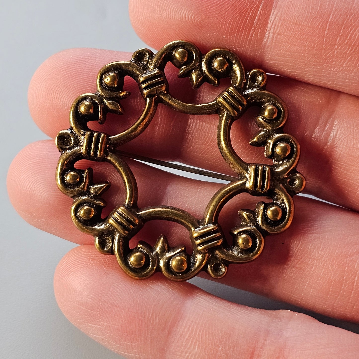 Ornate circular bronze brooch with swirling patterns and small spherical details.