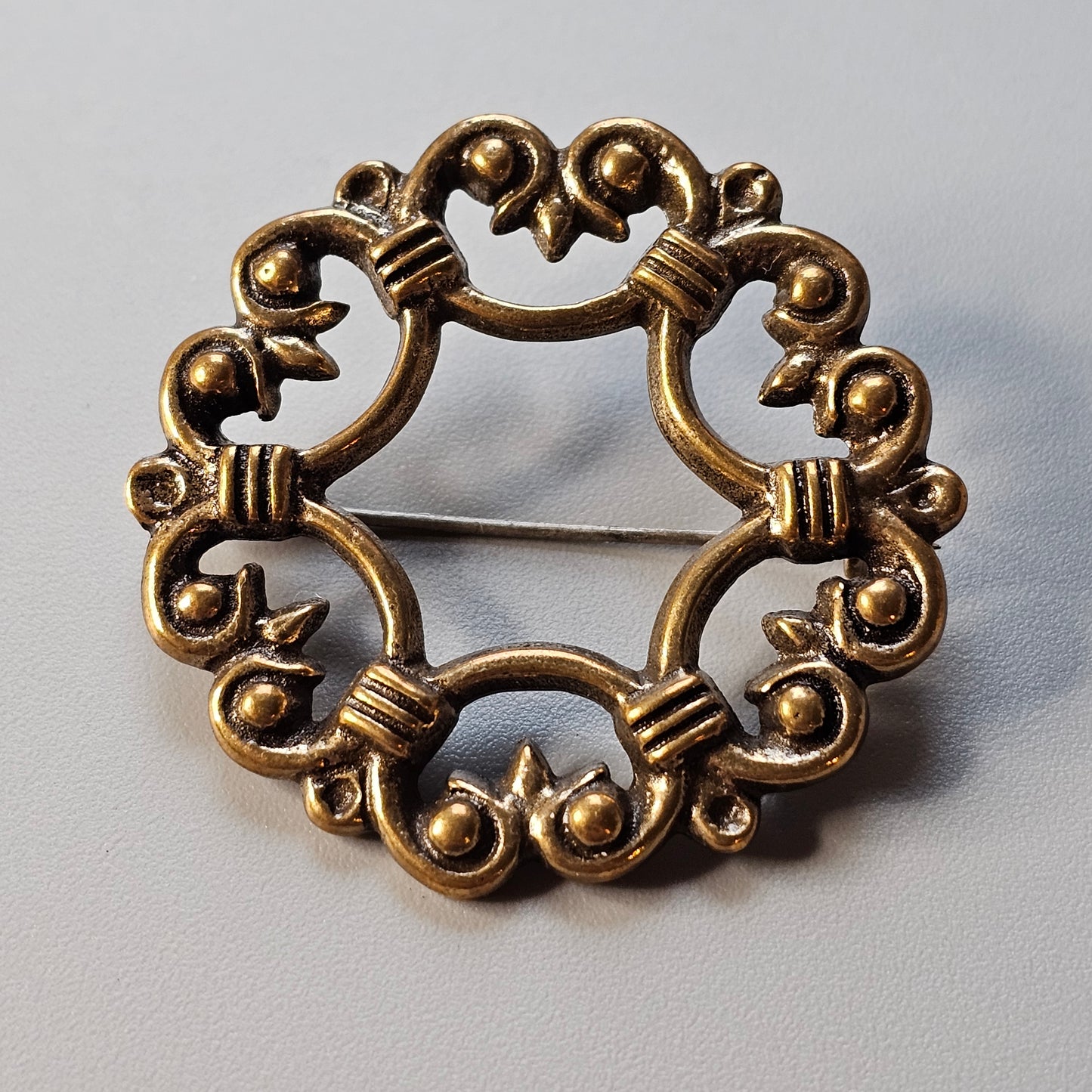 Ornate circular gold-toned brooch with intricate scrollwork and floral motifs.