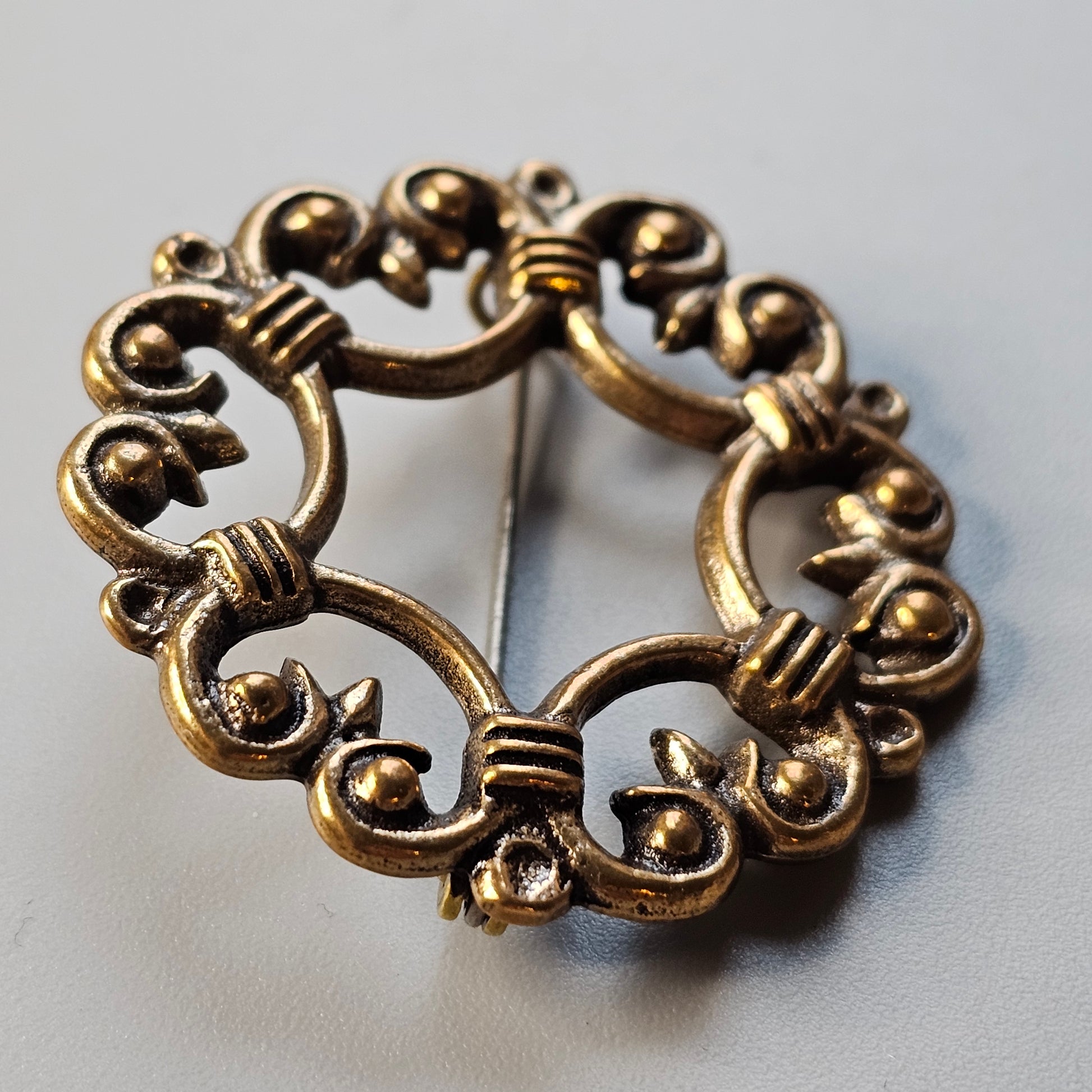 Ornate circular gold-toned metal brooch with floral and scroll designs.