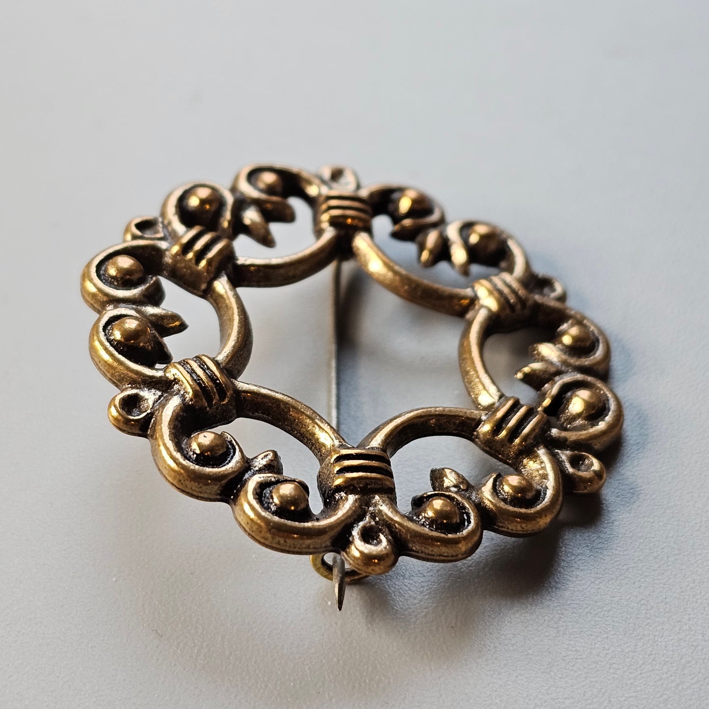 Ornate circular bronze brooch with intricate swirling patterns and small bead-like details.