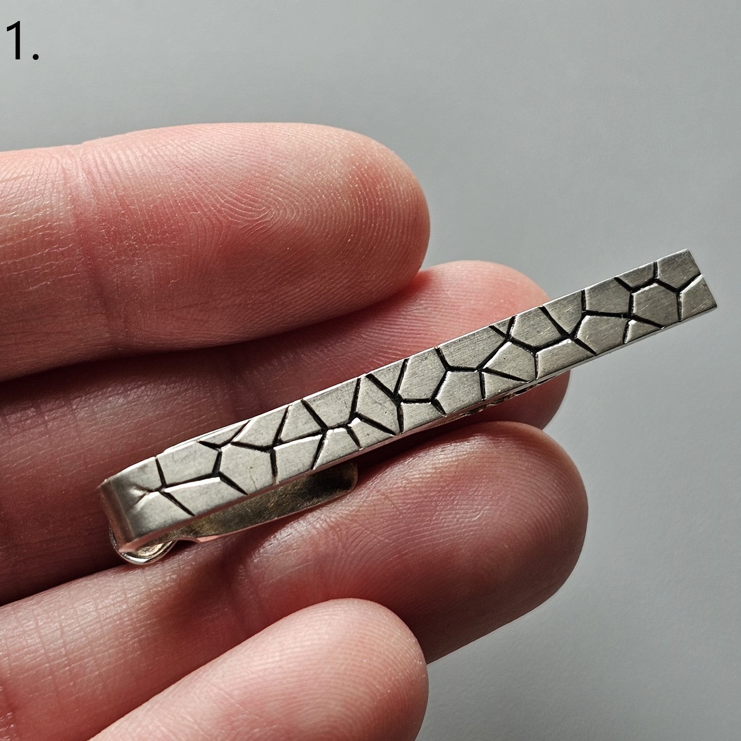 Metal tie clip with a geometric pattern resembling cracked or fractured shapes.