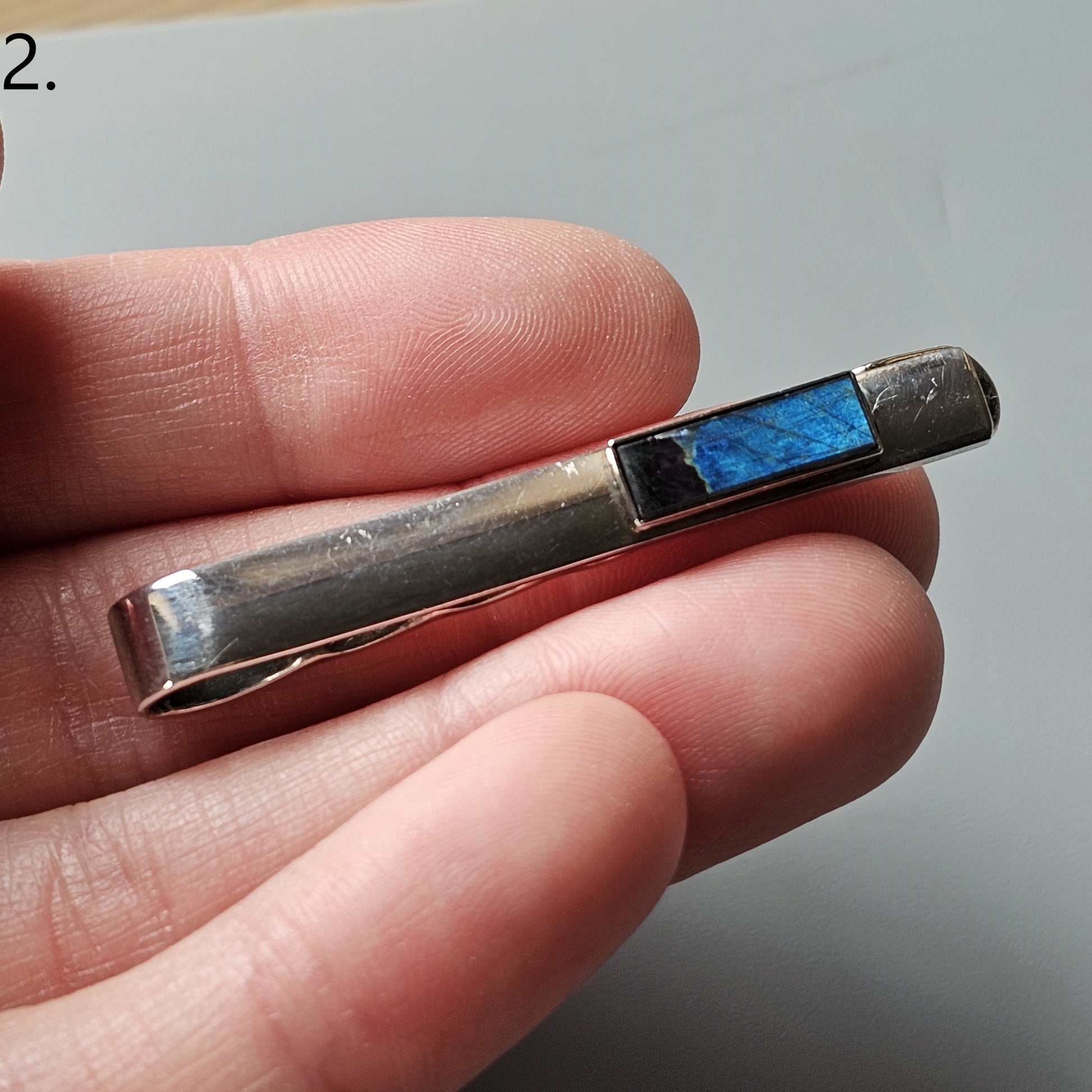 Metallic pen-like device with a blue cartridge visible at one end.