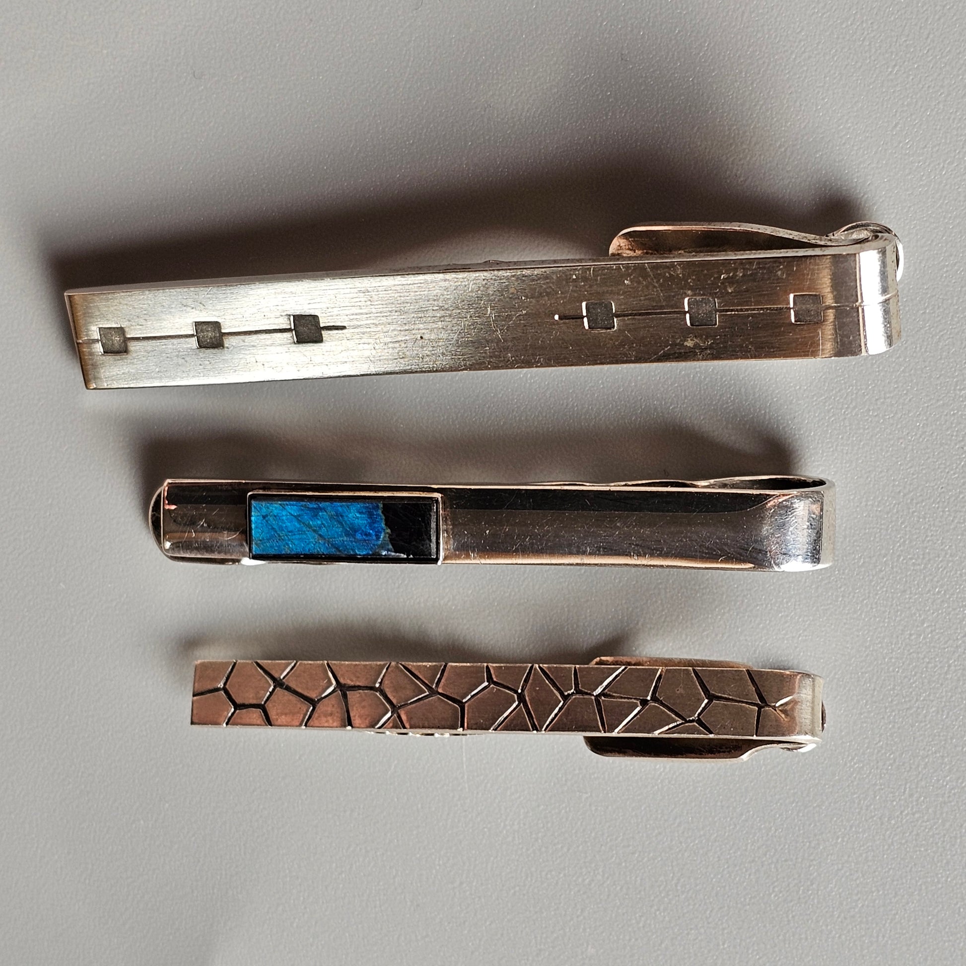 Three decorative tie clips or tie bars in different metallic designs.