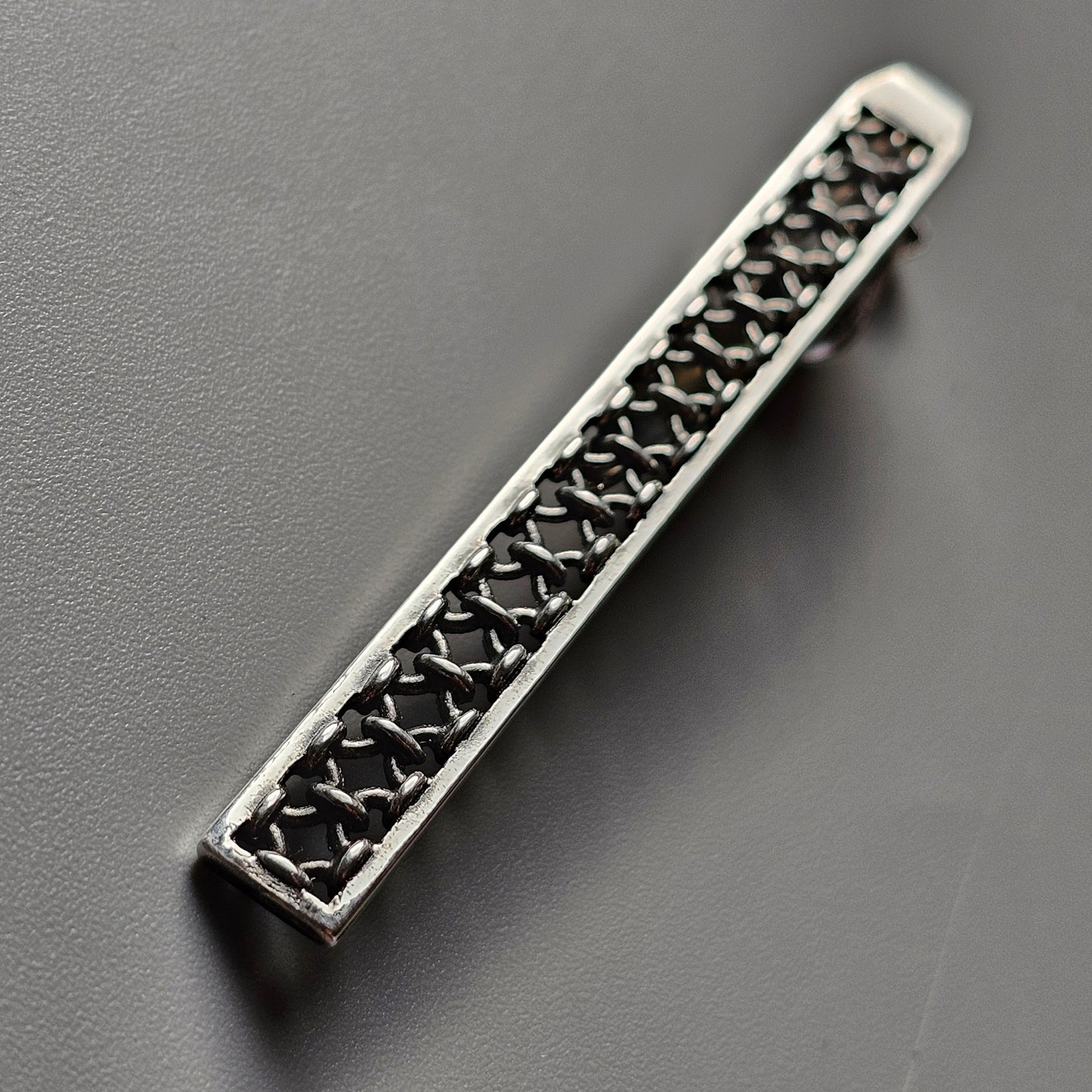 Elongated silver tie clip with intricate lattice pattern.