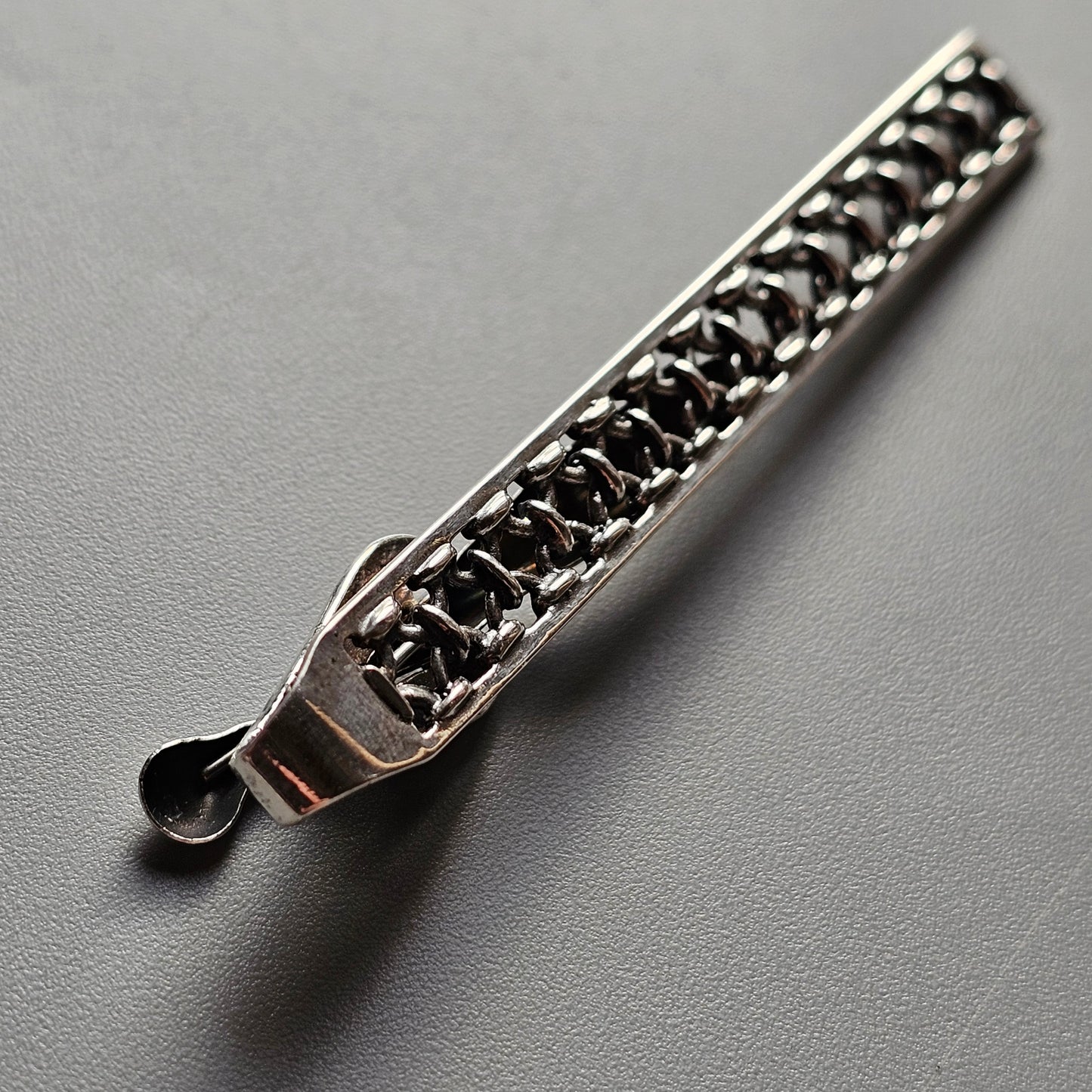 Metallic zipper pull with intricate chain-like design.