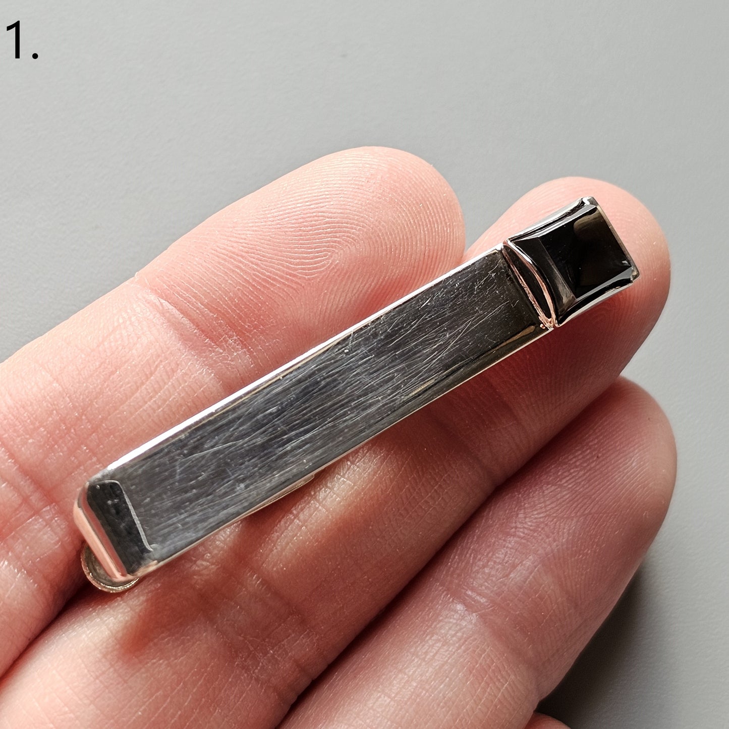 Metal tie clip or tie bar held between fingers.