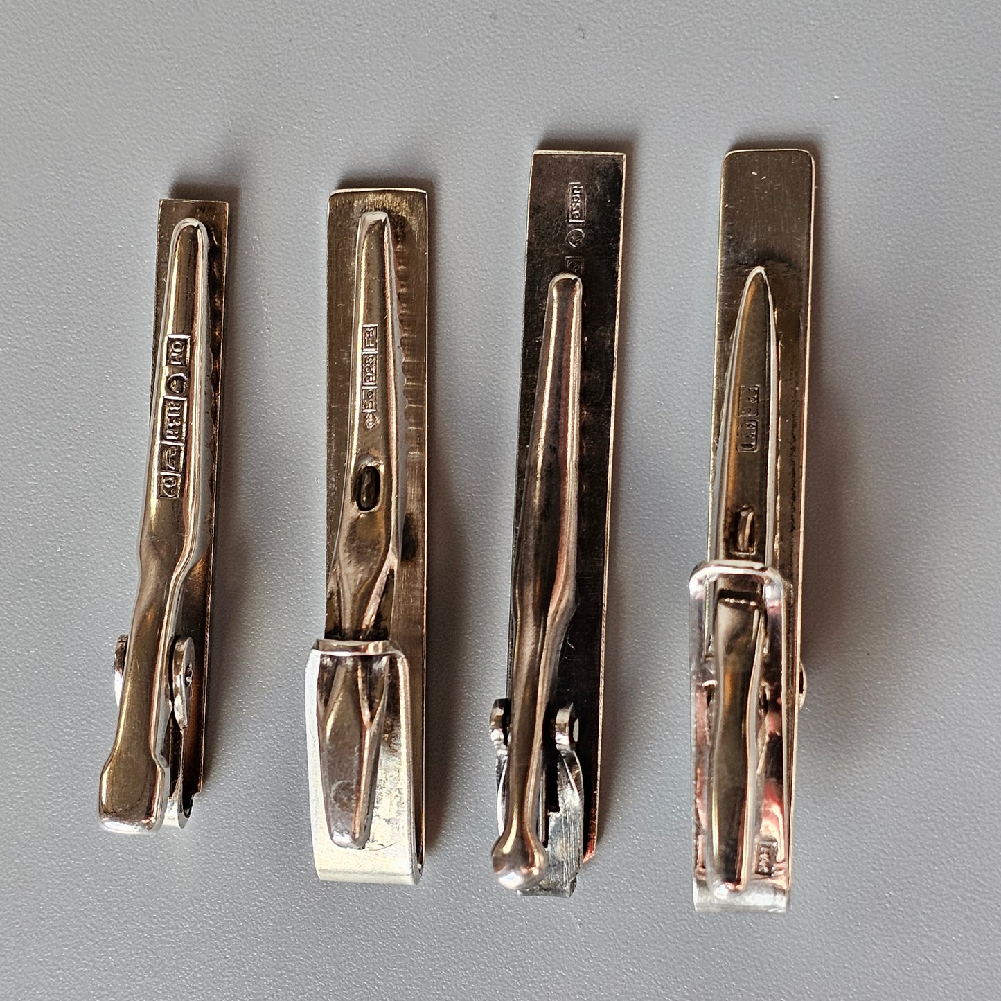 Four vintage metal clothespins or clothes pegs lined up side by side.