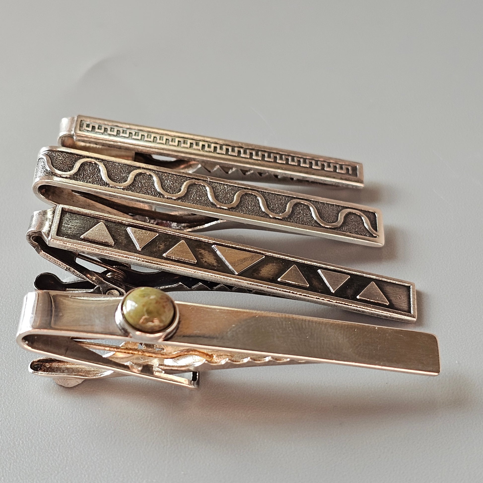 Collection of decorative metal tie clips with various engraved patterns and designs.