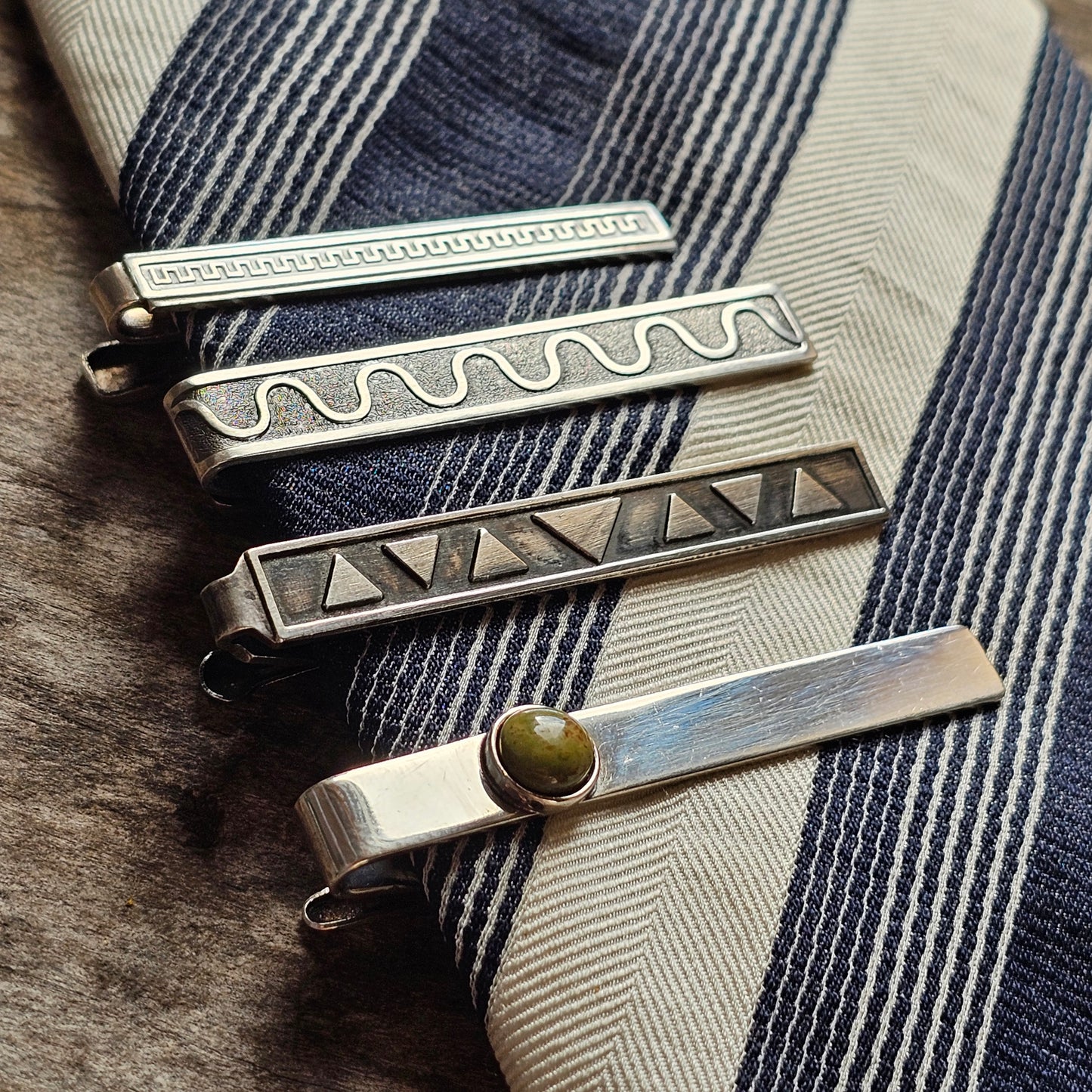 Collection of decorative metal tie clips with various engraved patterns.