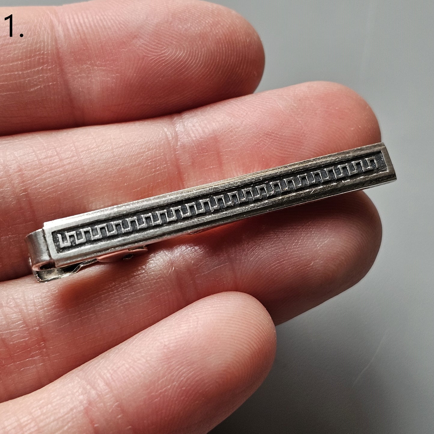 Silver tie clip with a decorative geometric pattern along its length.