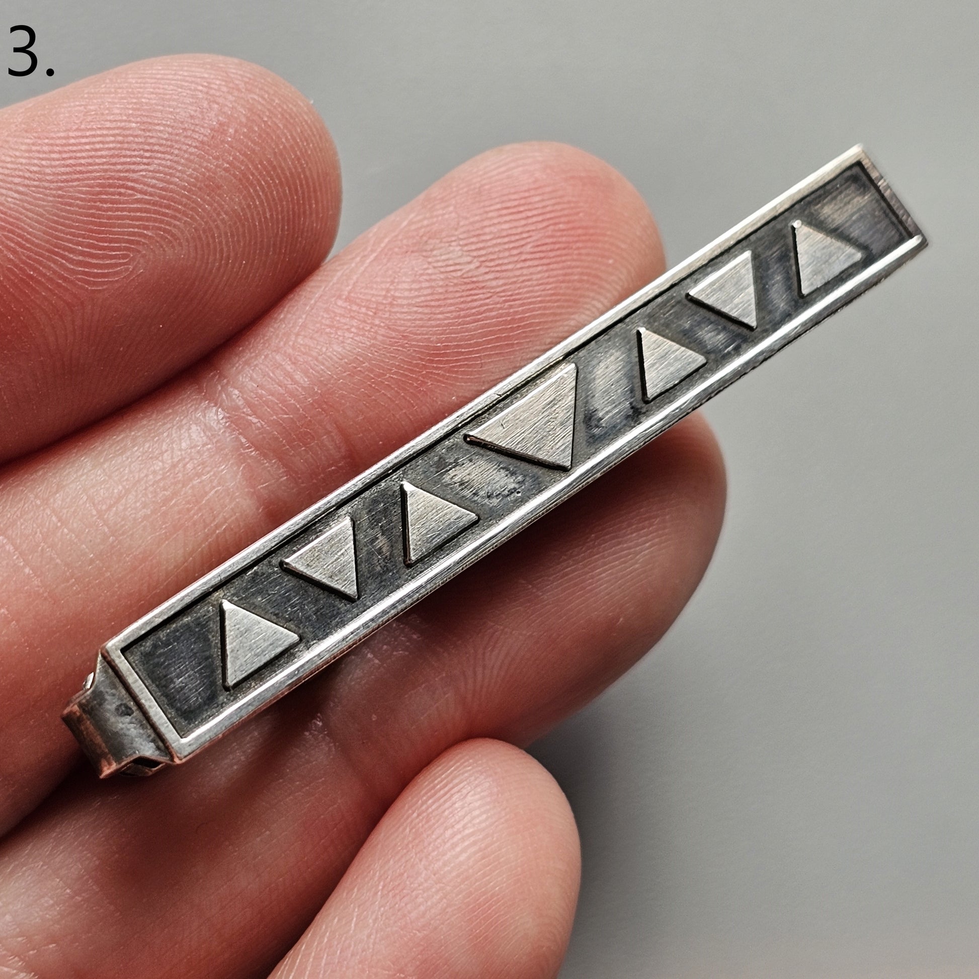 Silver tie clip with a geometric triangular pattern design.