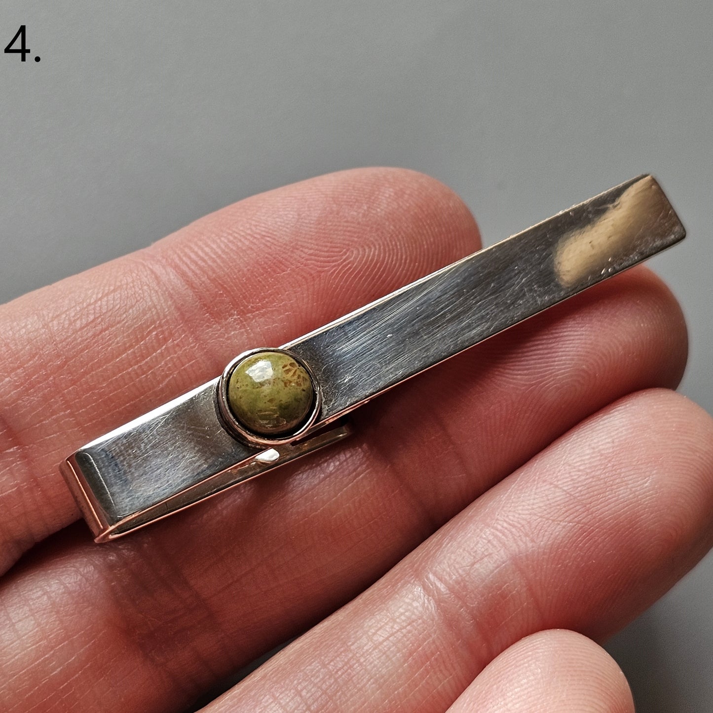 Metal tie clip with a small round gemstone or bead inset.