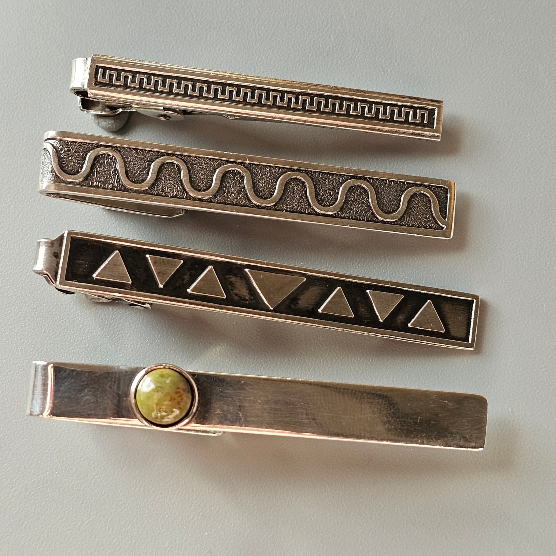 Set of four decorative metal tie clips with different engraved patterns.