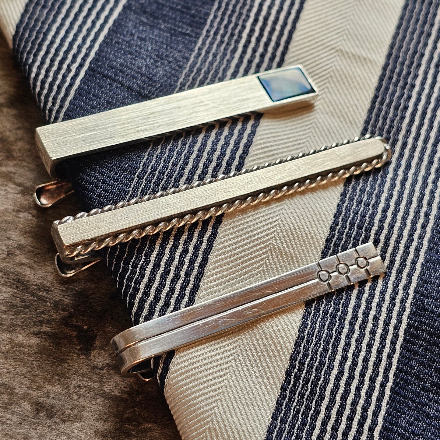 Three decorative metal tie clips with different designs.