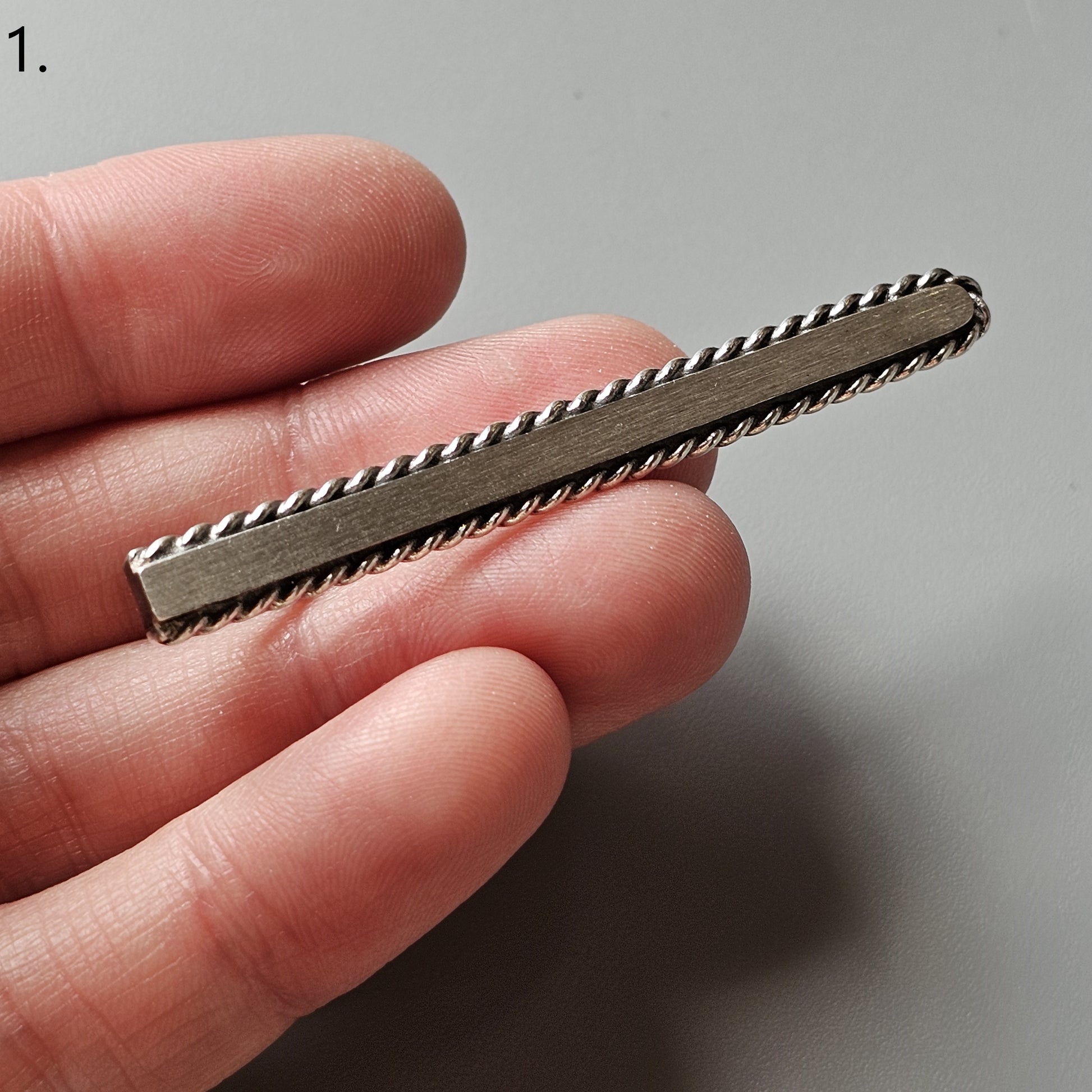 Elongated metal tie clip with twisted rope-like edges.