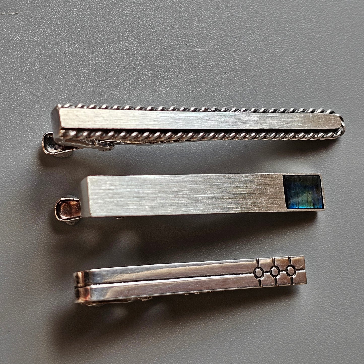 Three silver-toned tie clips with different decorative patterns.